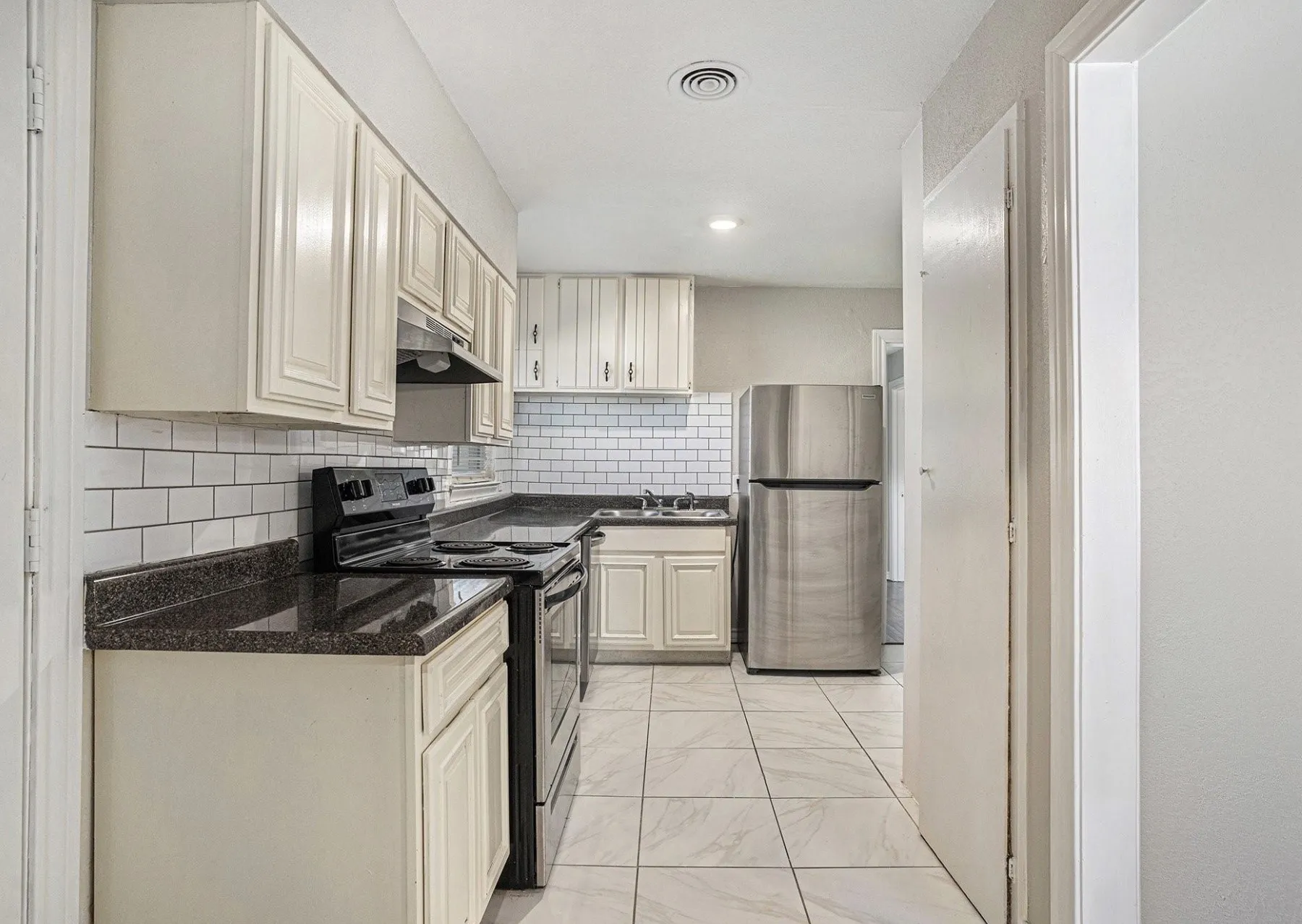 Kitchen featuring subway tile backsplash, cream-colored cabinetry, and dark countertops