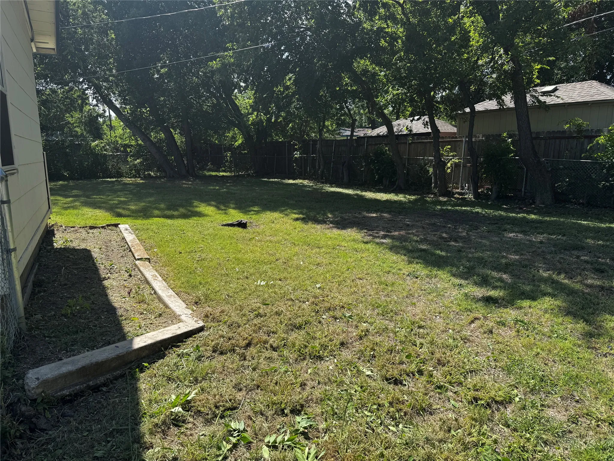 Spacious backyard featuring a grass lawn, mature perimeter trees, and wood fencing
