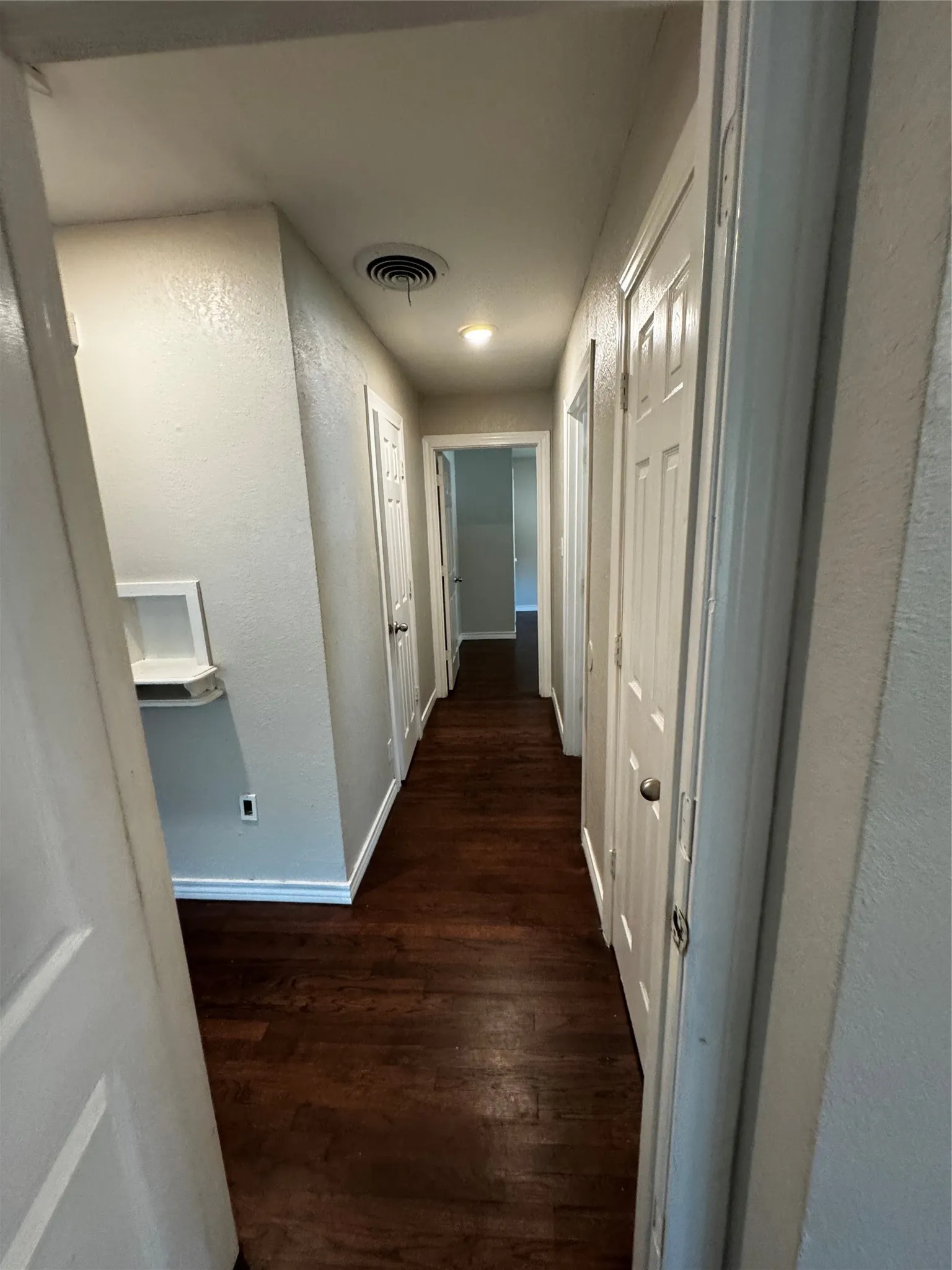 Hallway featuring wood-finish flooring, white baseboards, and light gray wall paint