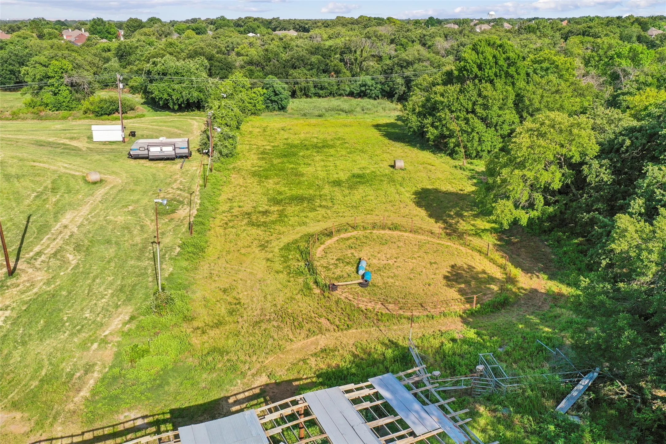 Expansive grass lot featuring mature tree lines, a circular graded area, and overhead utility lines