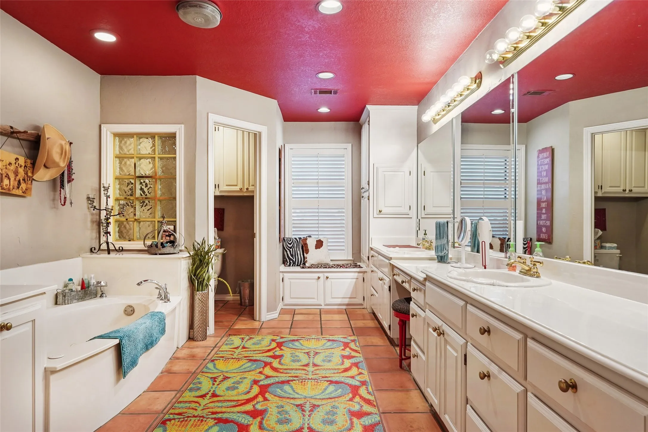 Spacious bathroom featuring terracotta-style flooring, a built-in soaking tub, and a vanity with dual sinks