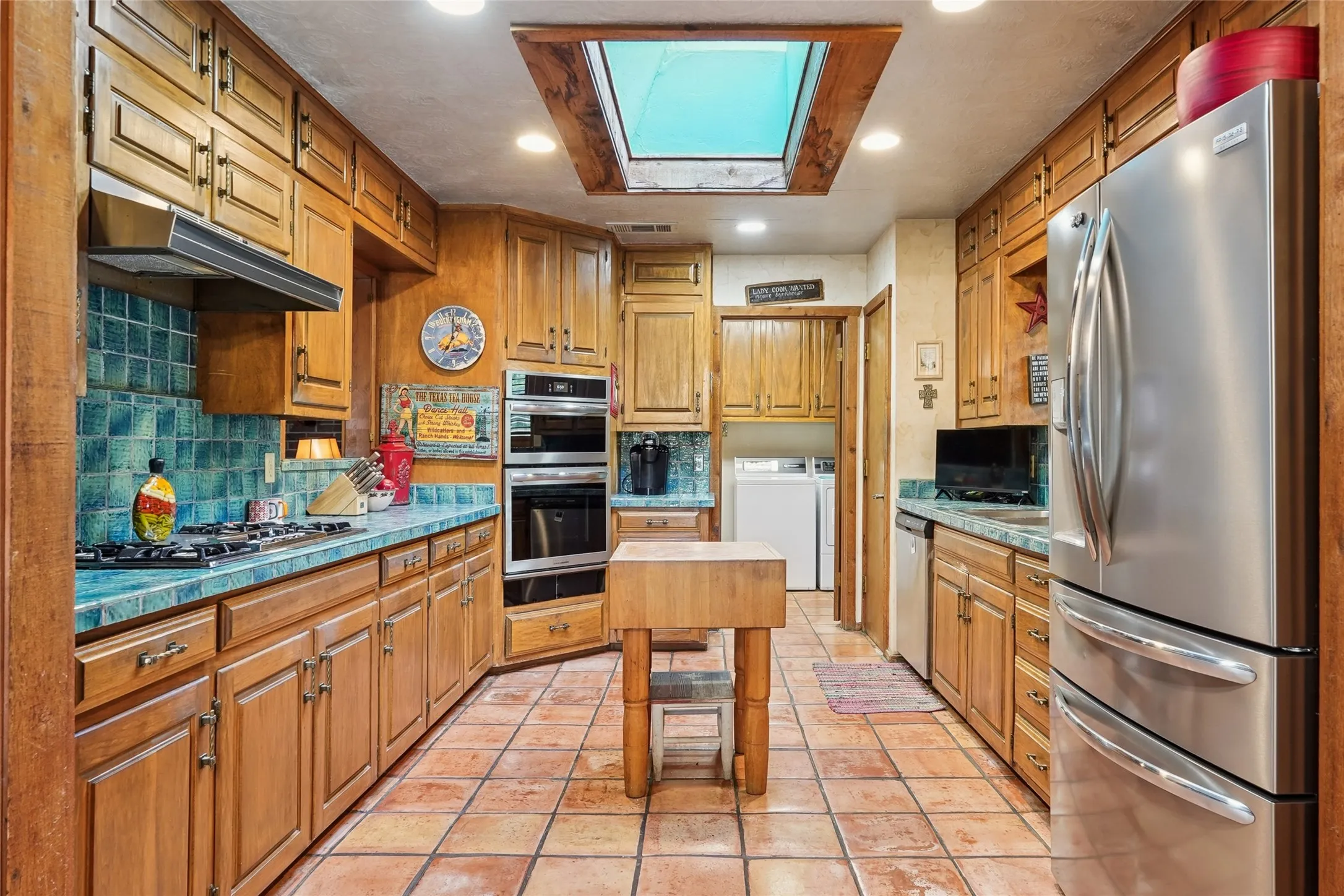 Kitchen featuring a skylight, tile flooring, wood cabinetry, tile countertops, and stainless steel appliances