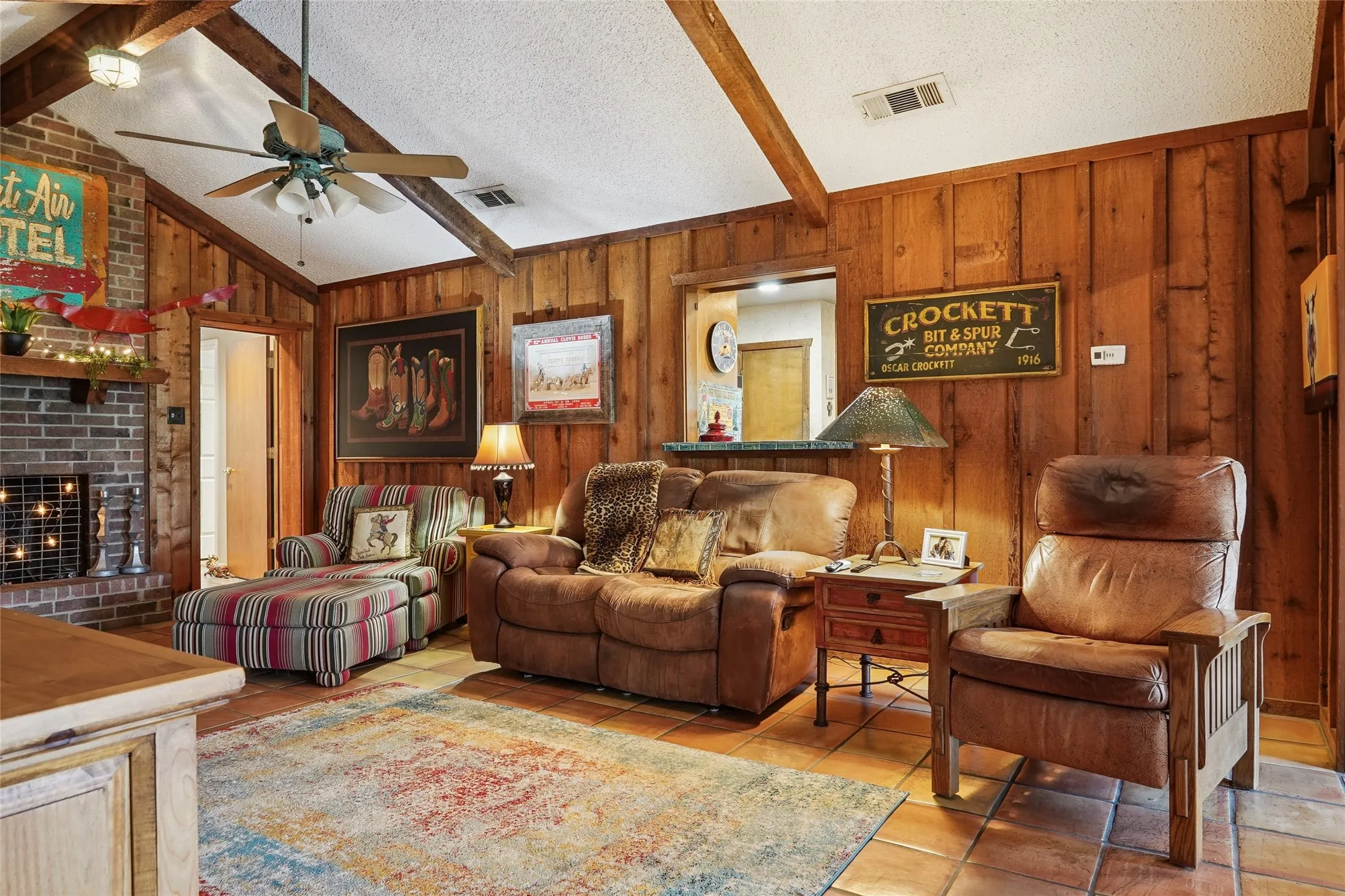 Living area featuring wood paneling, a brick fireplace with a mantle, and exposed ceiling beams