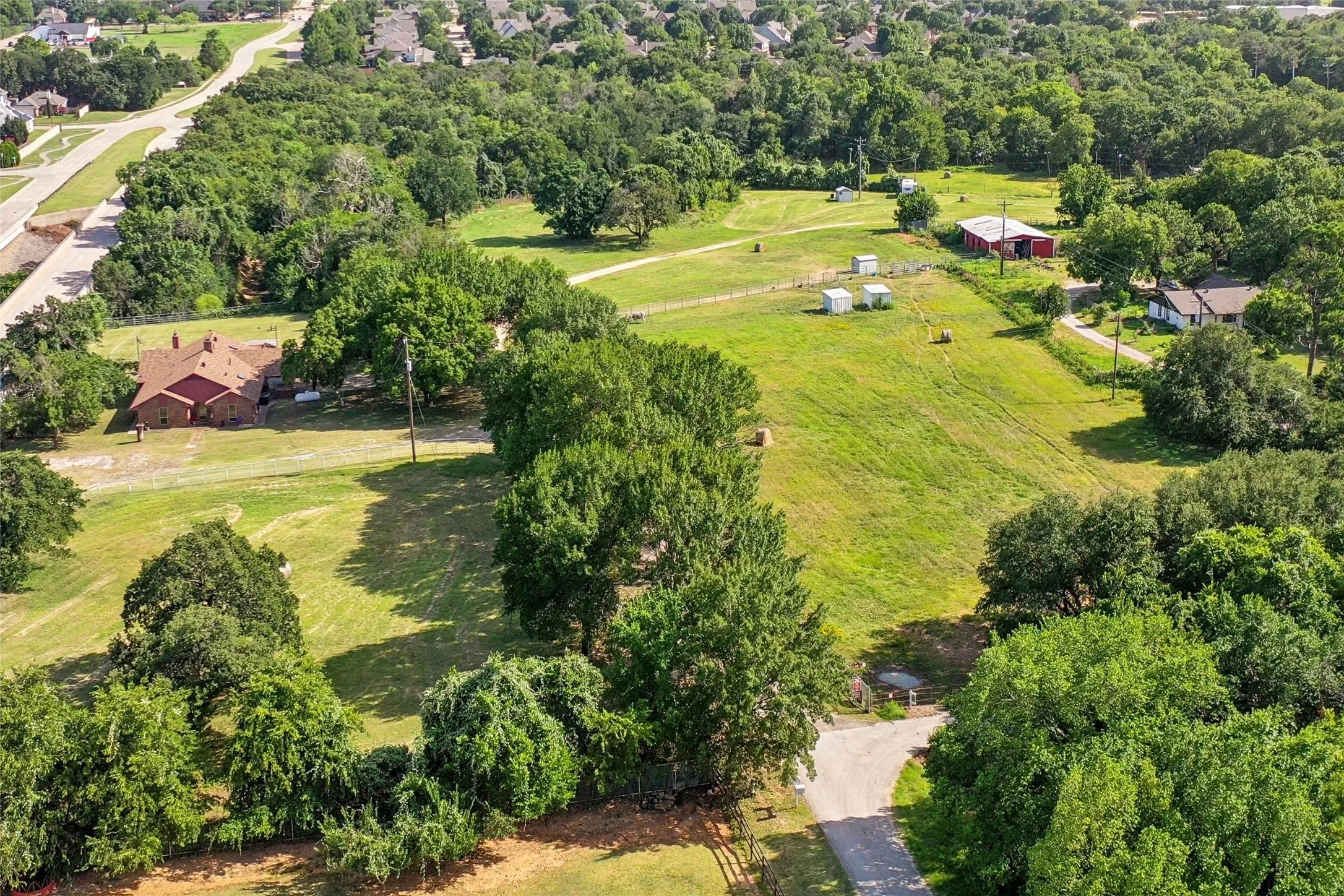 Expansive property featuring a red brick residence with a multi-gabled roof, a red barn structure, established trees, substantial green space, and a paved driveway