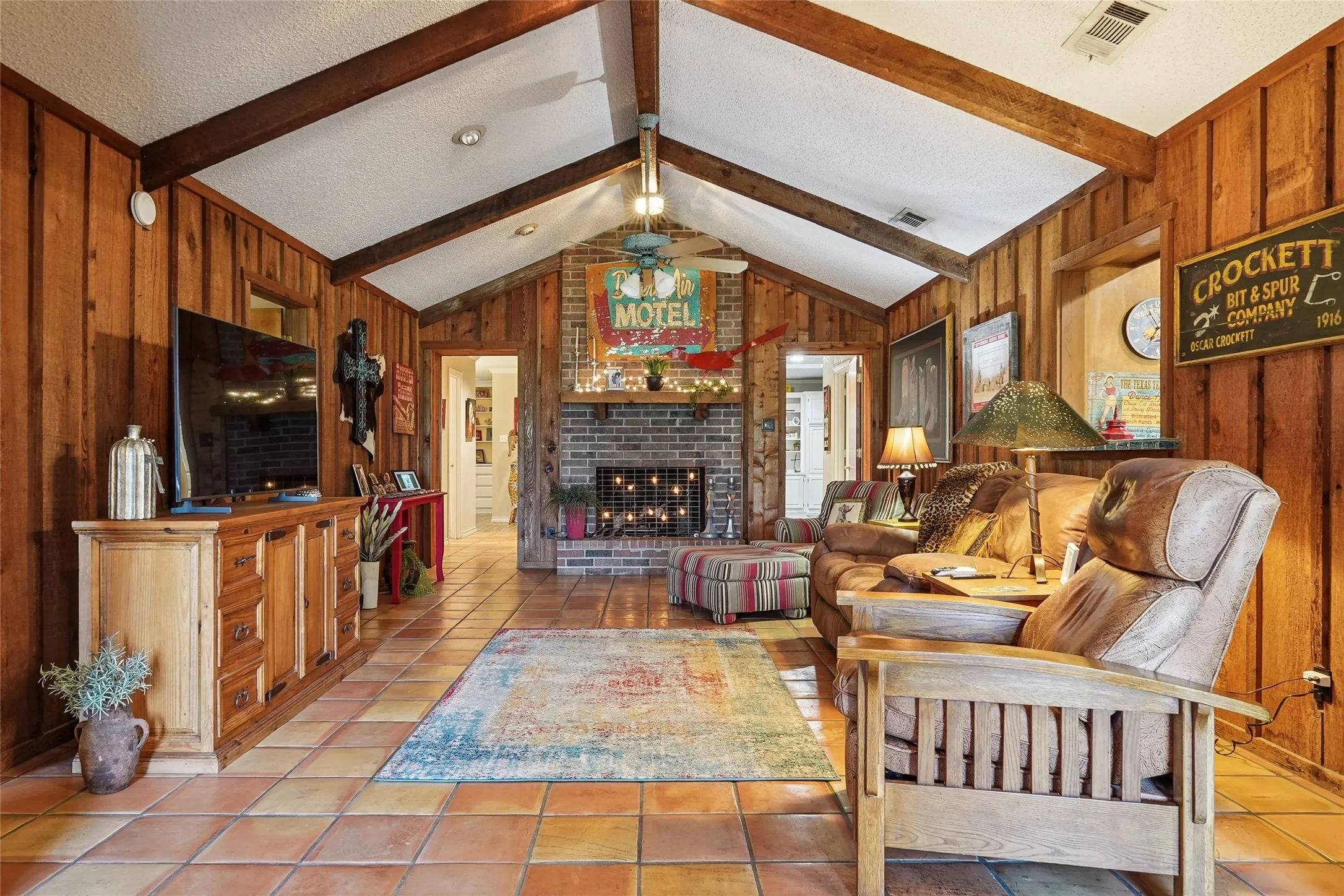 Living area featuring a vaulted ceiling with exposed wood beams, plank wood wall paneling, and terra cotta tile flooring