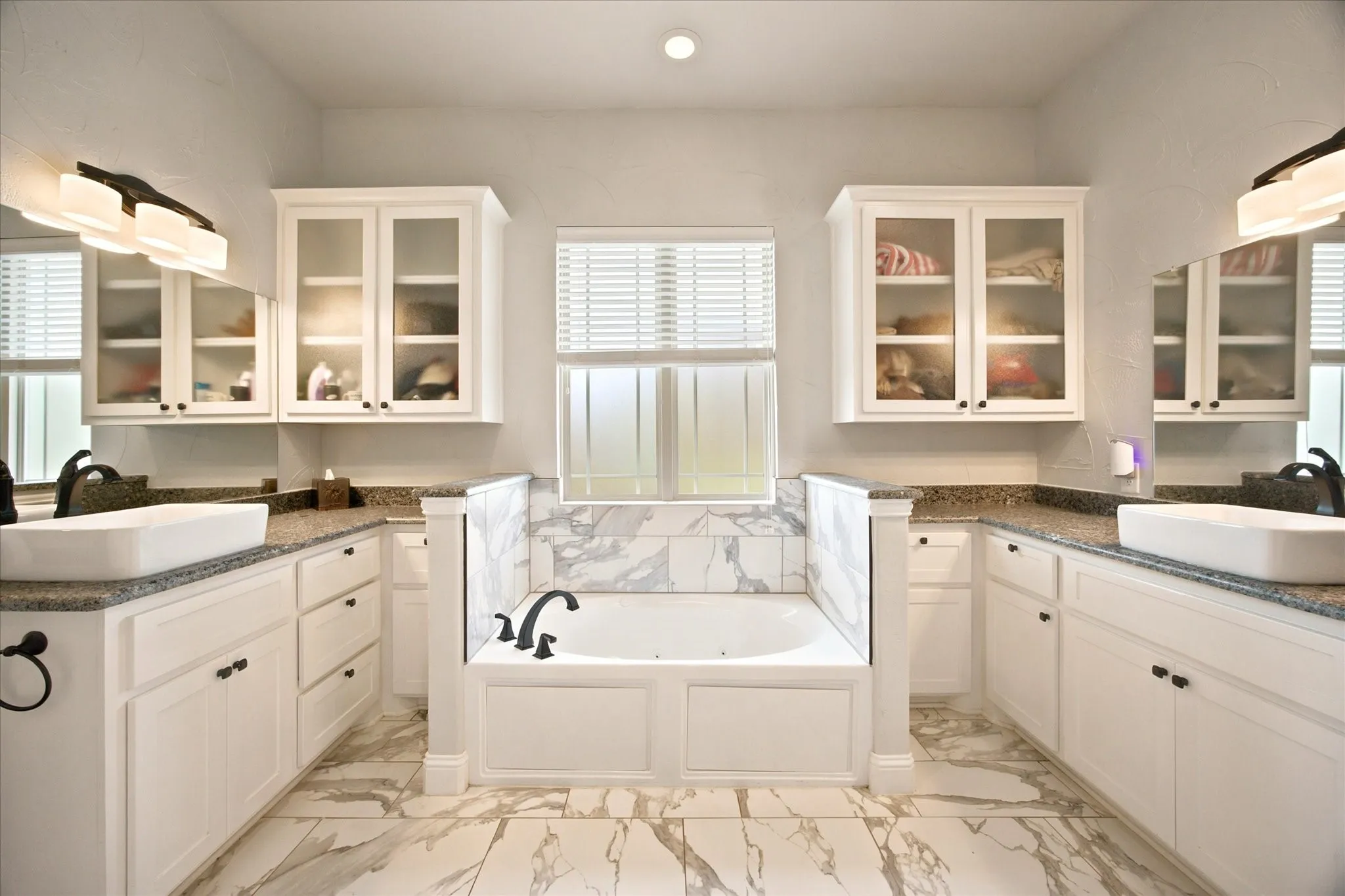 Soaking tub with marble-style surround, flanked by white cabinetry