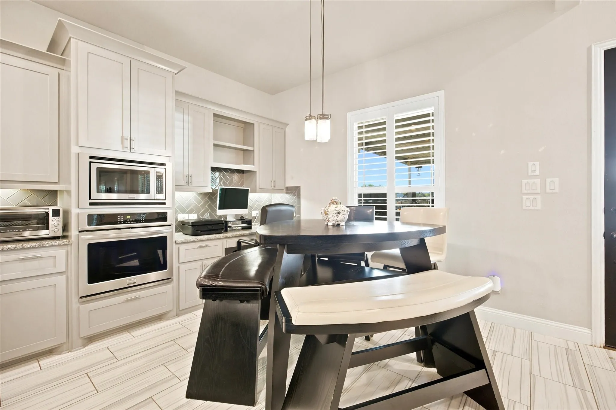 Integrated kitchen and office area featuring light-toned cabinetry, stainless steel built-in appliances, a herringbone tile backsplash, and wood-finish flooring