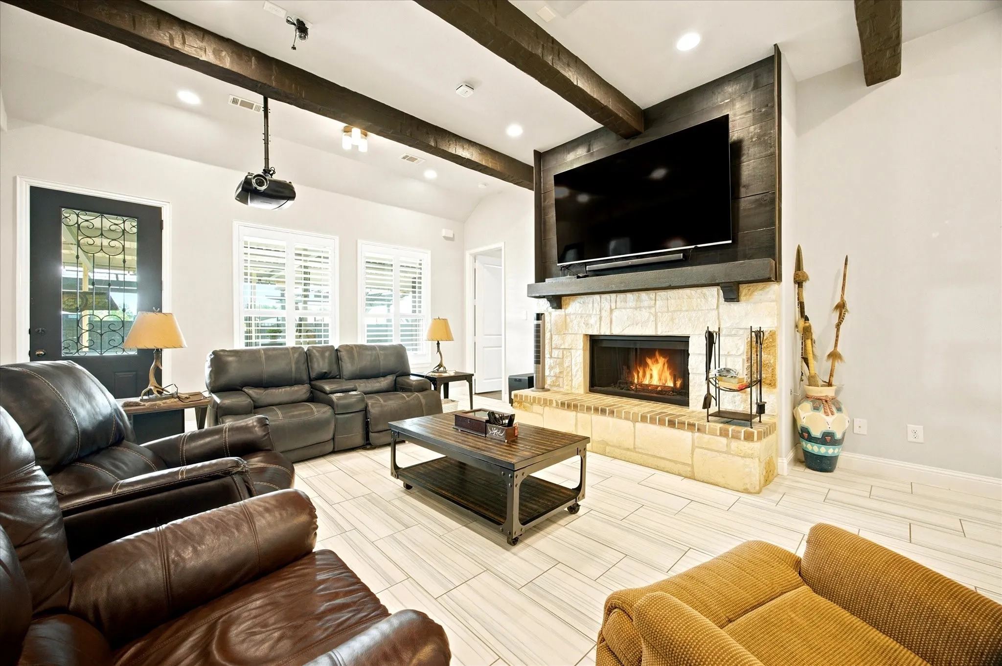 Spacious living area featuring a stone fireplace with a wood mantel, vaulted ceiling with exposed beams, recessed lighting, and light-toned wood-finish flooring