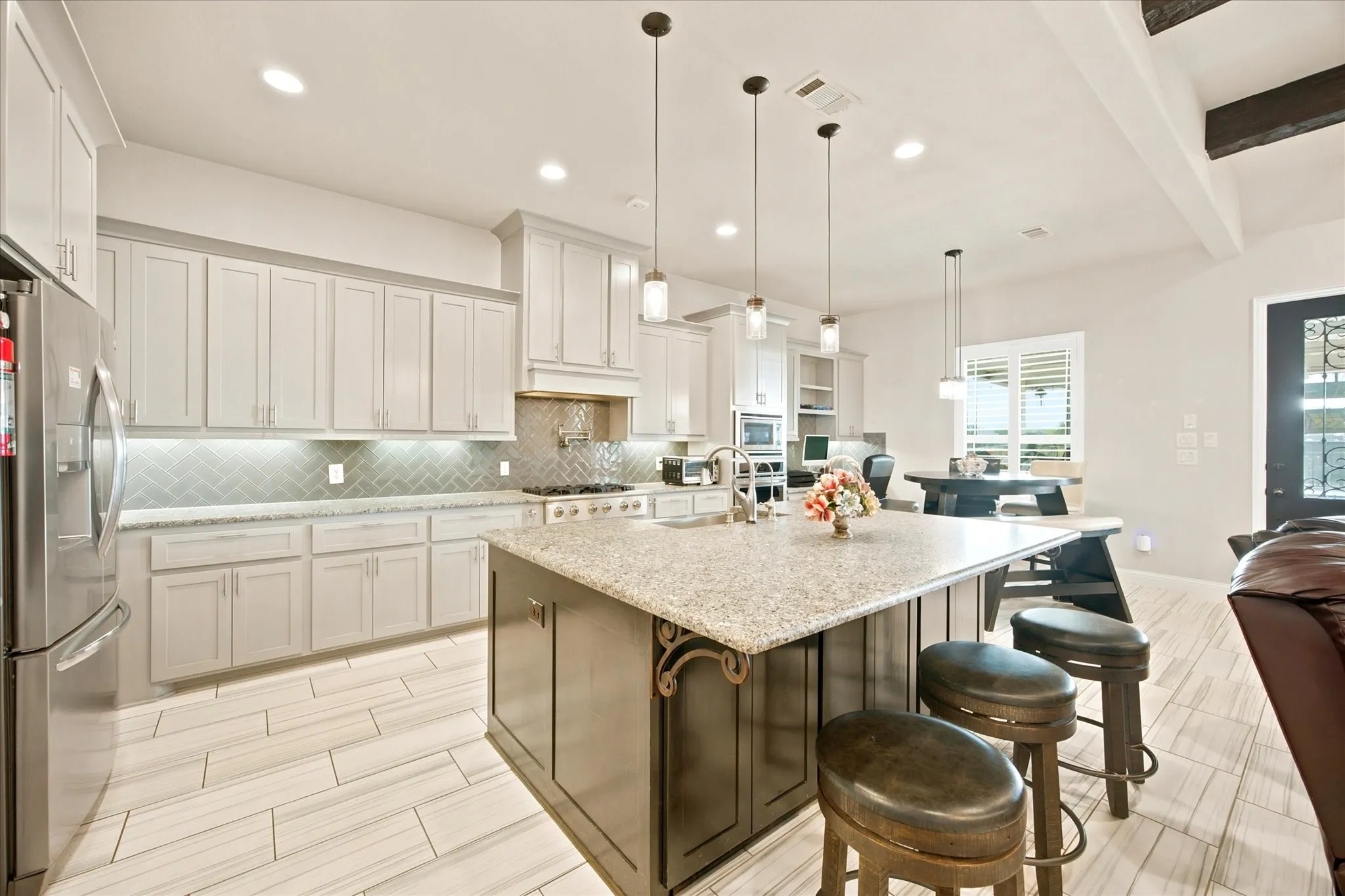Gourmet kitchen featuring a large central island with granite countertop, stainless steel appliances, light gray cabinetry, a herringbone tile backsplash, and light wood-look flooring