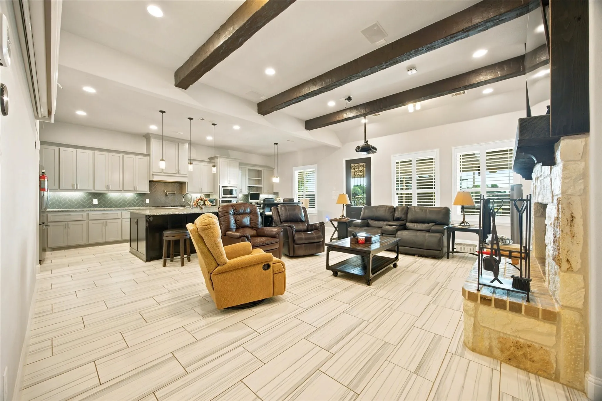 Open-concept living space featuring vaulted ceilings with exposed wood beams, a stone and brick fireplace, and wood-finish tile flooring