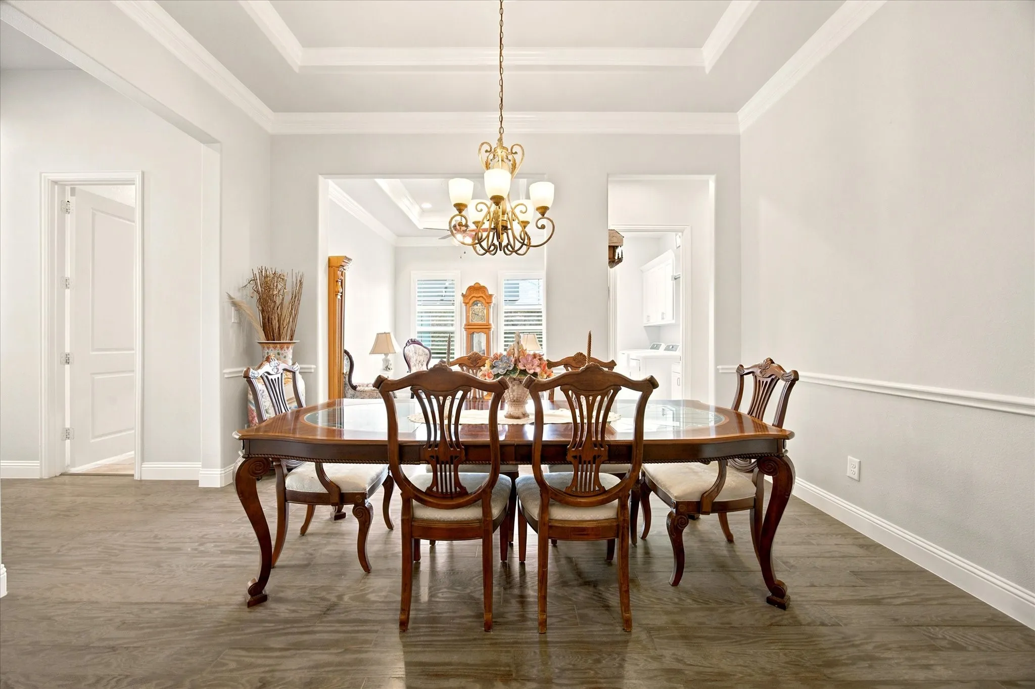 Formal dining room featuring a tray ceiling with a brass chandelier, wood-finish flooring, and white baseboards