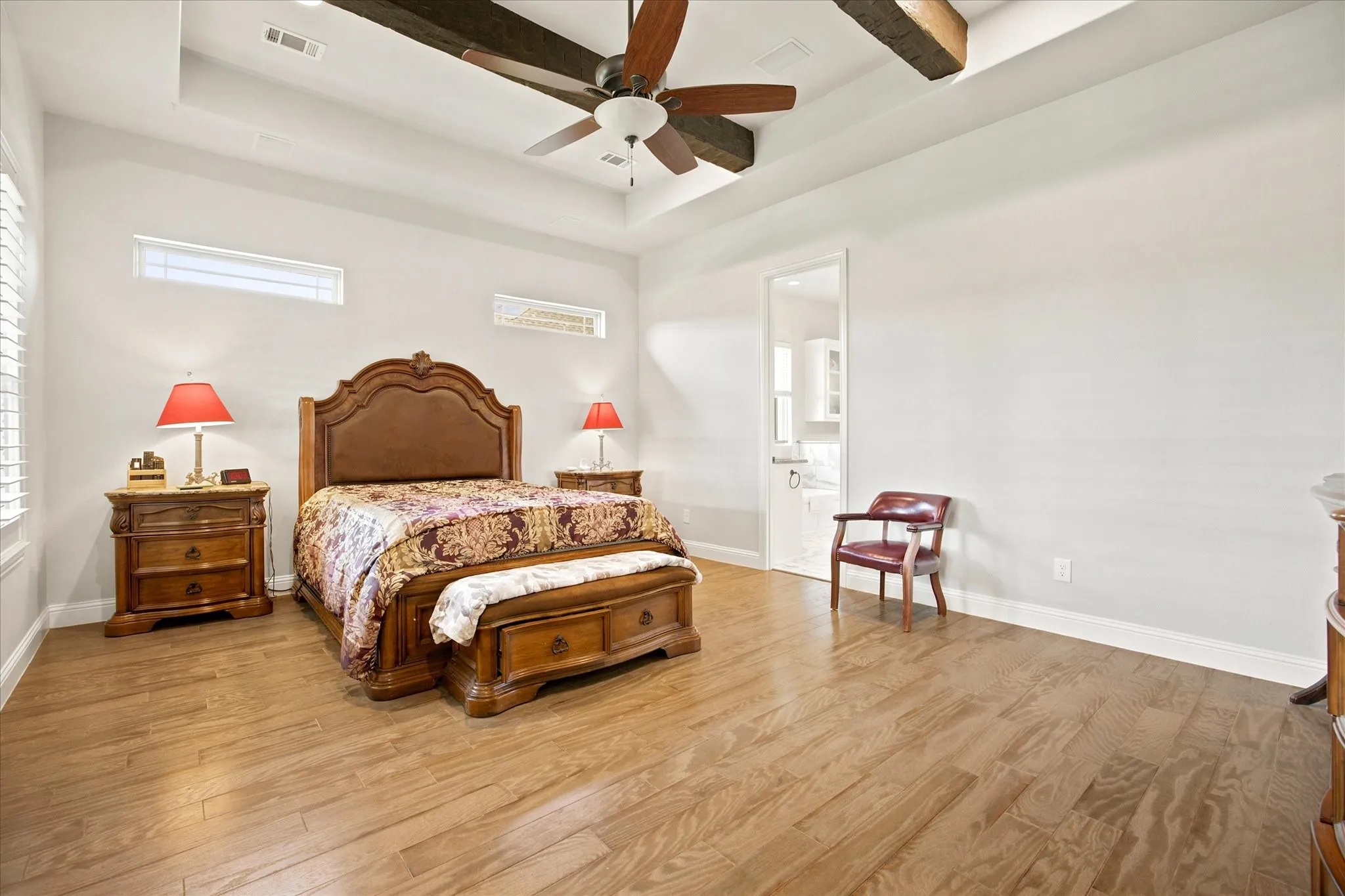 Spacious interior featuring wood-finish flooring, a tray ceiling with exposed wood beams, and a ceiling fan