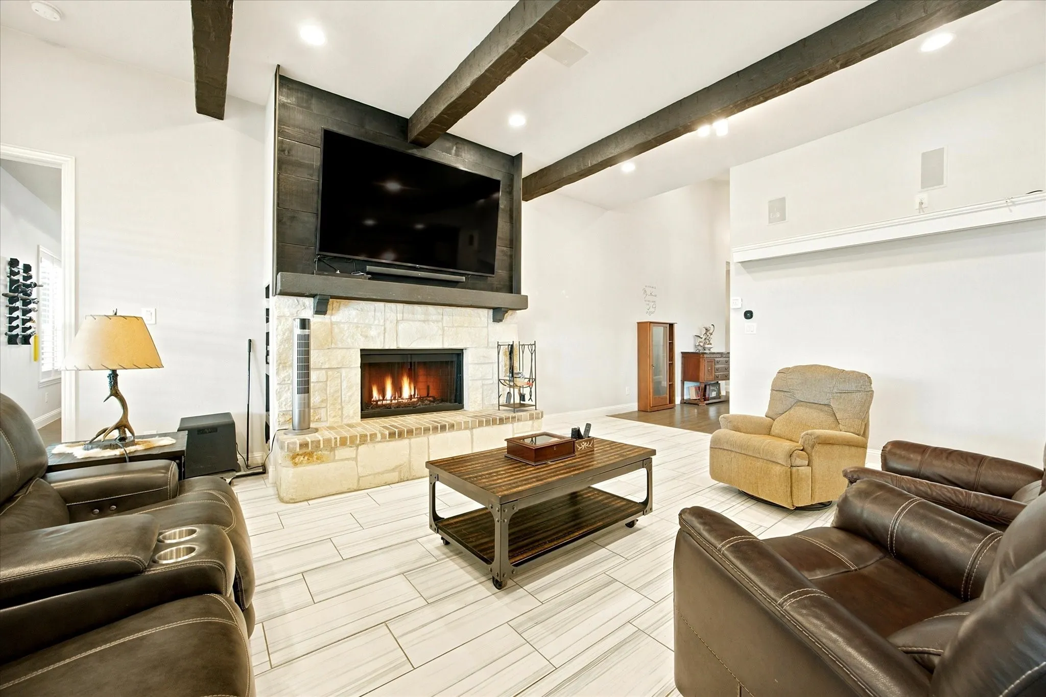 Living space featuring a stone-clad fireplace, wood-beamed ceiling, recessed lighting, and tile flooring