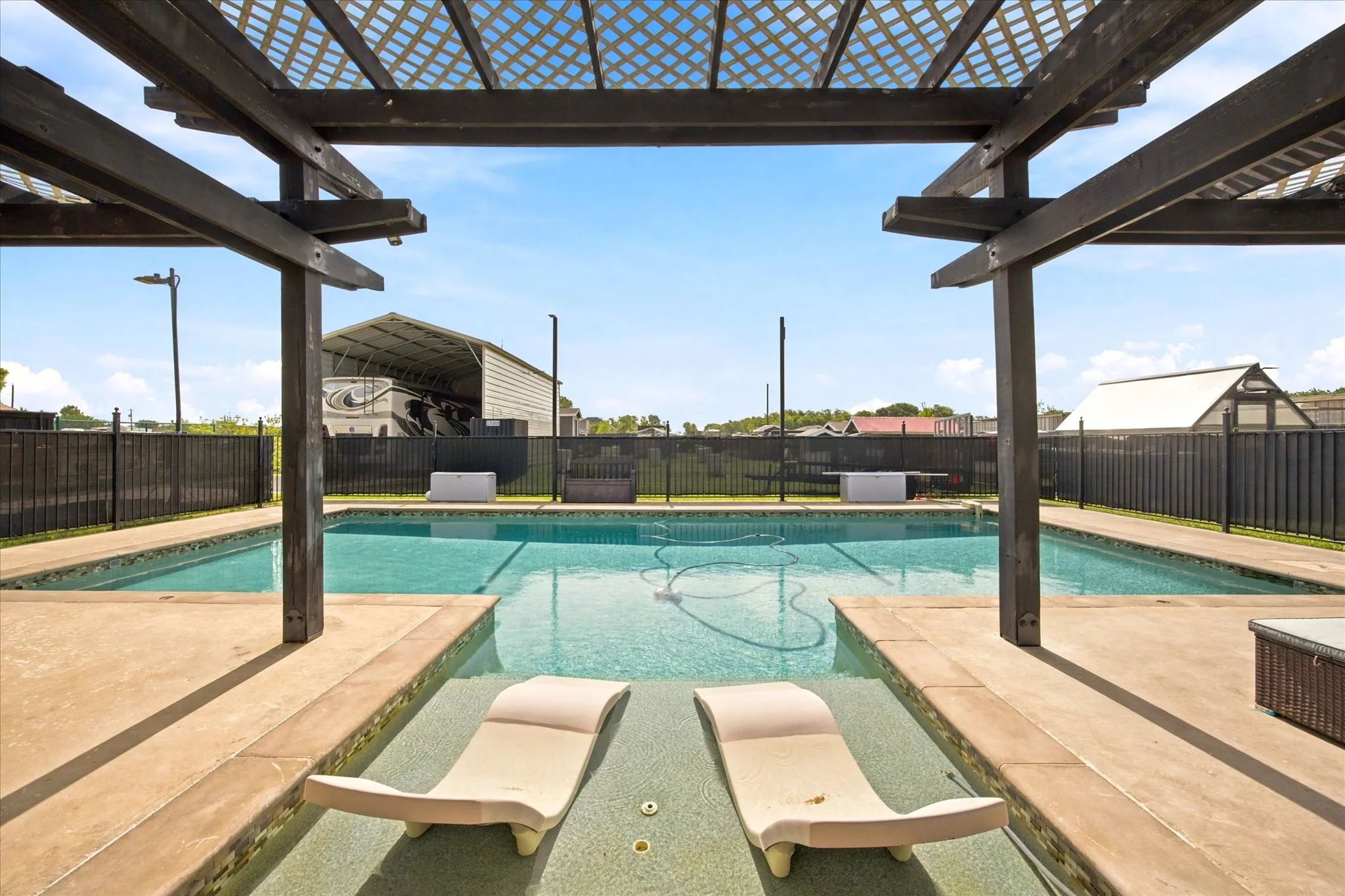 Pergola-covered patio area featuring a swimming pool with integrated sun shelves
