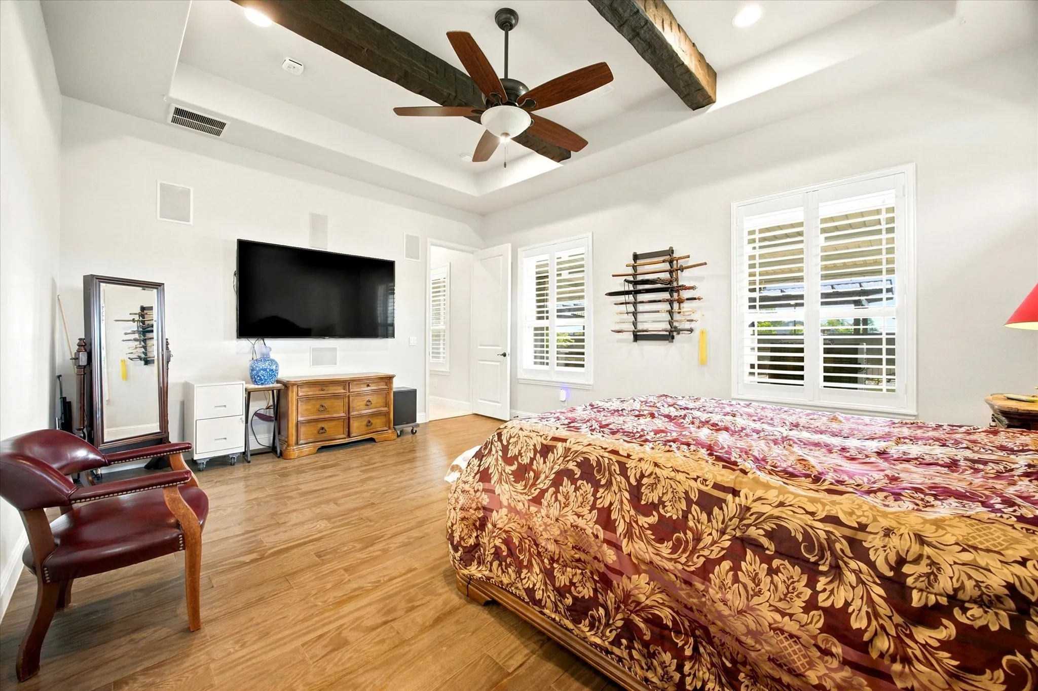 Spacious room featuring wood-finish flooring, a tray ceiling with exposed wood beams, and a ceiling fan