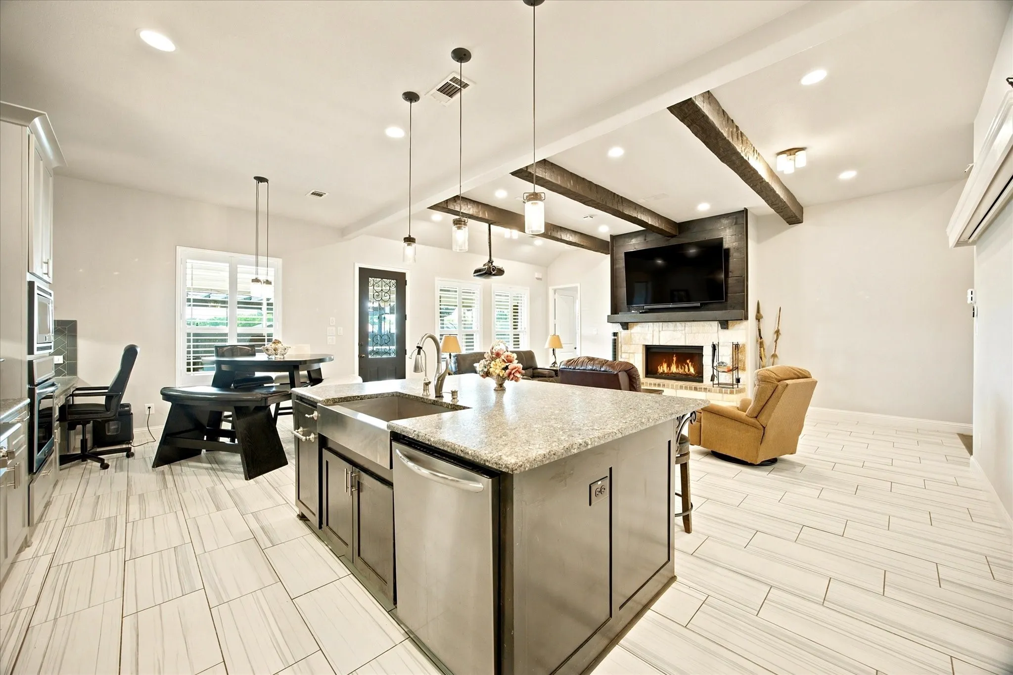 Open-concept living space featuring a central kitchen island with a farmhouse sink, stainless steel appliances, and a light-toned countertop