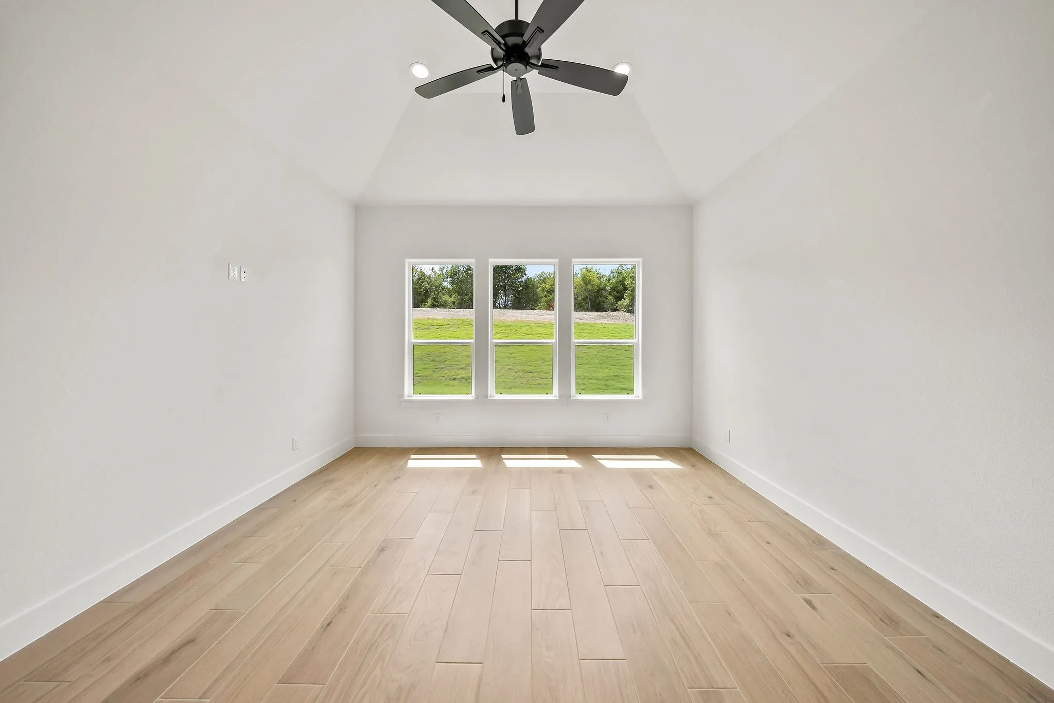 Vaulted ceiling with a black ceiling fan featuring recessed lighting, three large windows, wood-finish flooring, and white baseboards