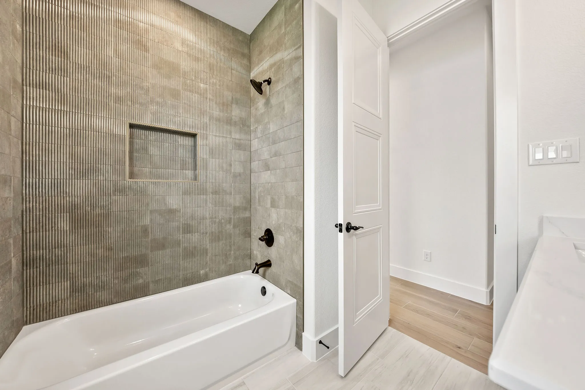 Bathtub with tiled surround featuring a textured accent panel, integrated niche, and matte black fixtures