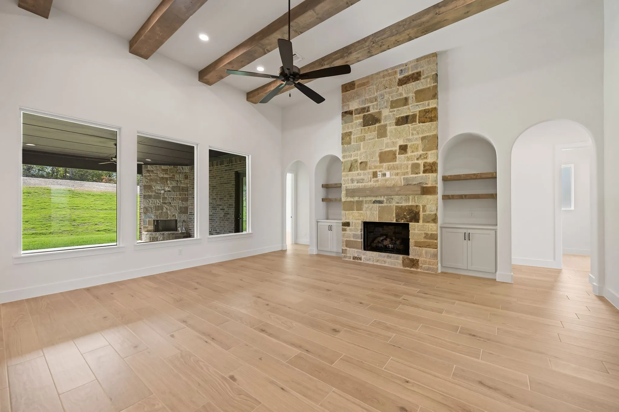 Spacious living area featuring a stone-clad fireplace with wood mantle, vaulted ceiling with exposed wood beams, and recessed lighting