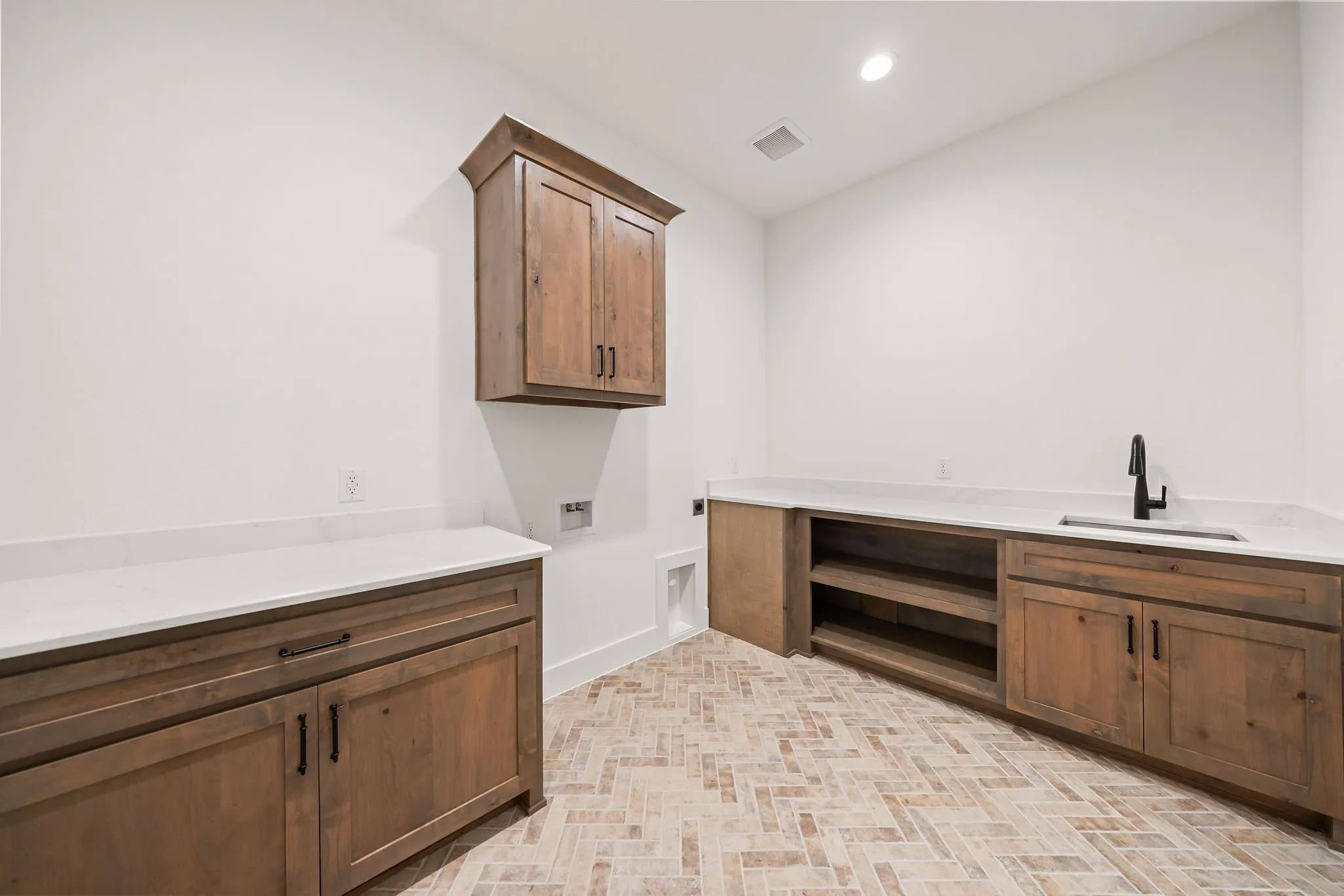 Utility room featuring herringbone tile flooring, custom wood cabinetry, white countertops, built-in shelving, and an undermount sink with a matte black faucet