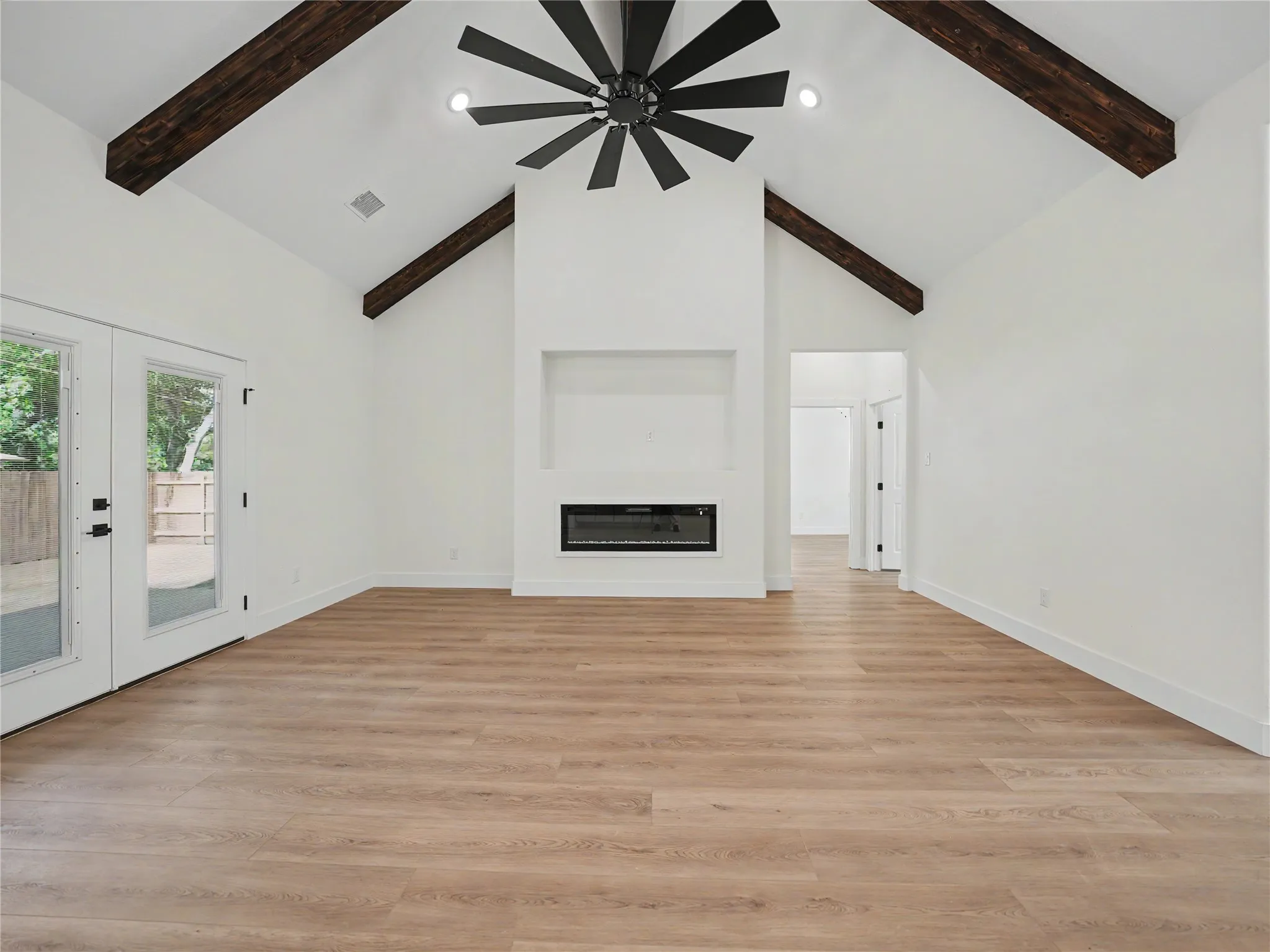 Vaulted ceiling with exposed wood beams, a modern fireplace, wood-finish flooring, and French doors
