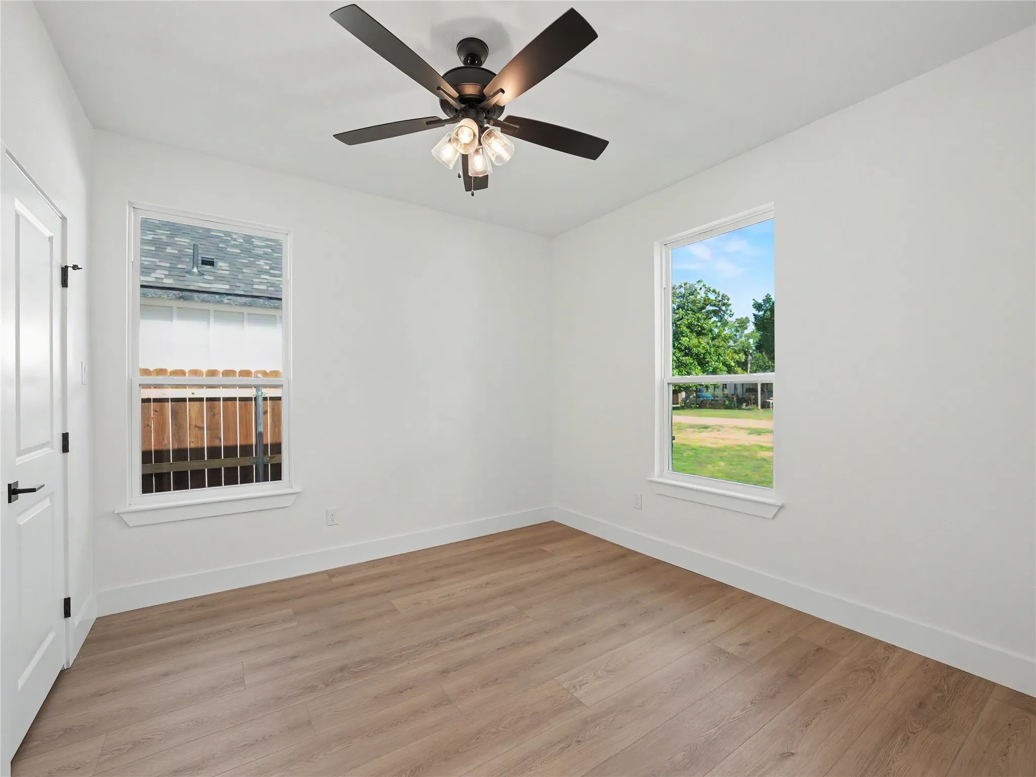 Bright room featuring wood-finish flooring, two large windows, a ceiling fan with light fixture, white walls, and white baseboards