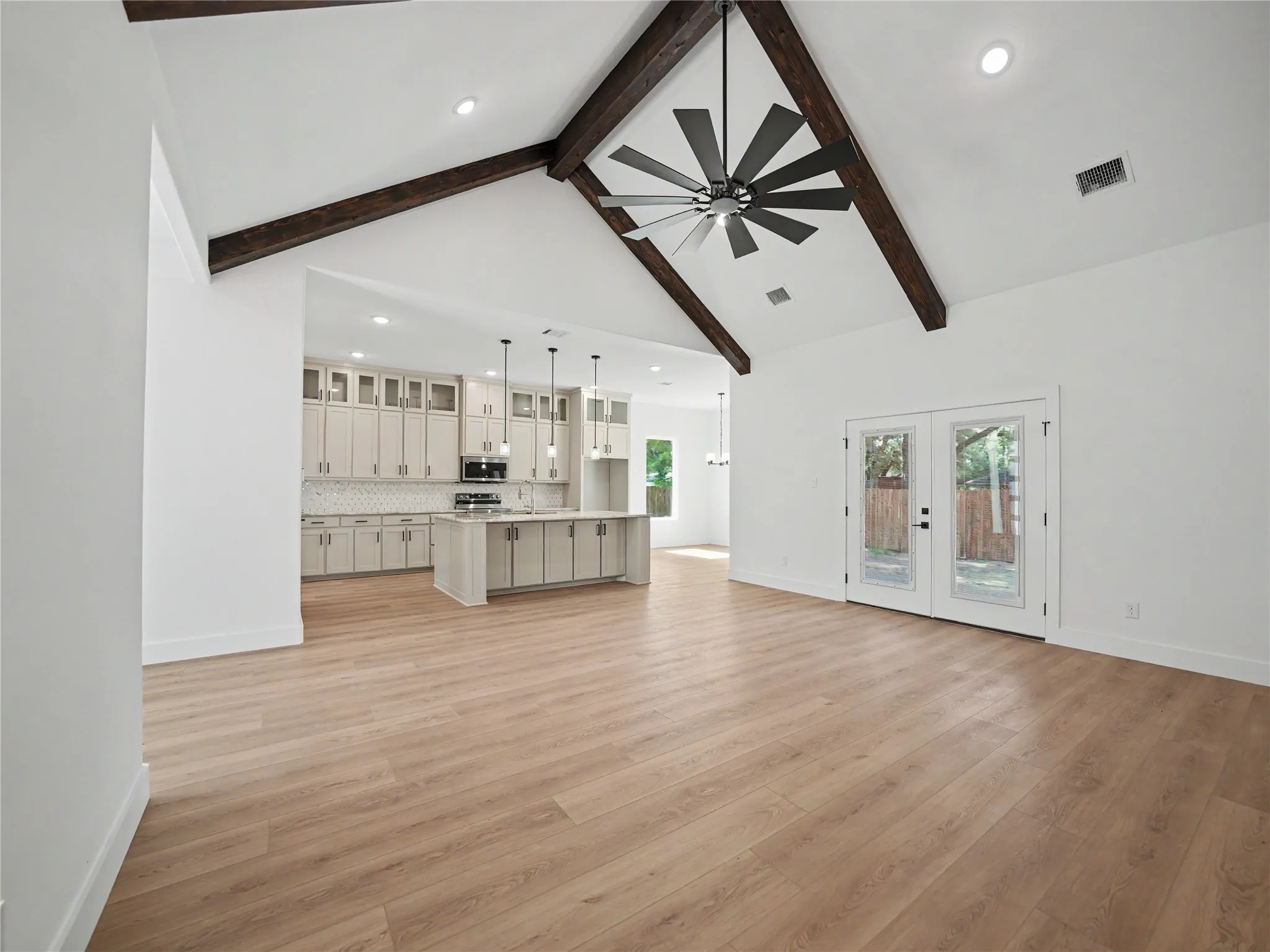 Expansive living area featuring vaulted ceilings with exposed wood beams, a modern ceiling fan, and light wood-finish flooring
