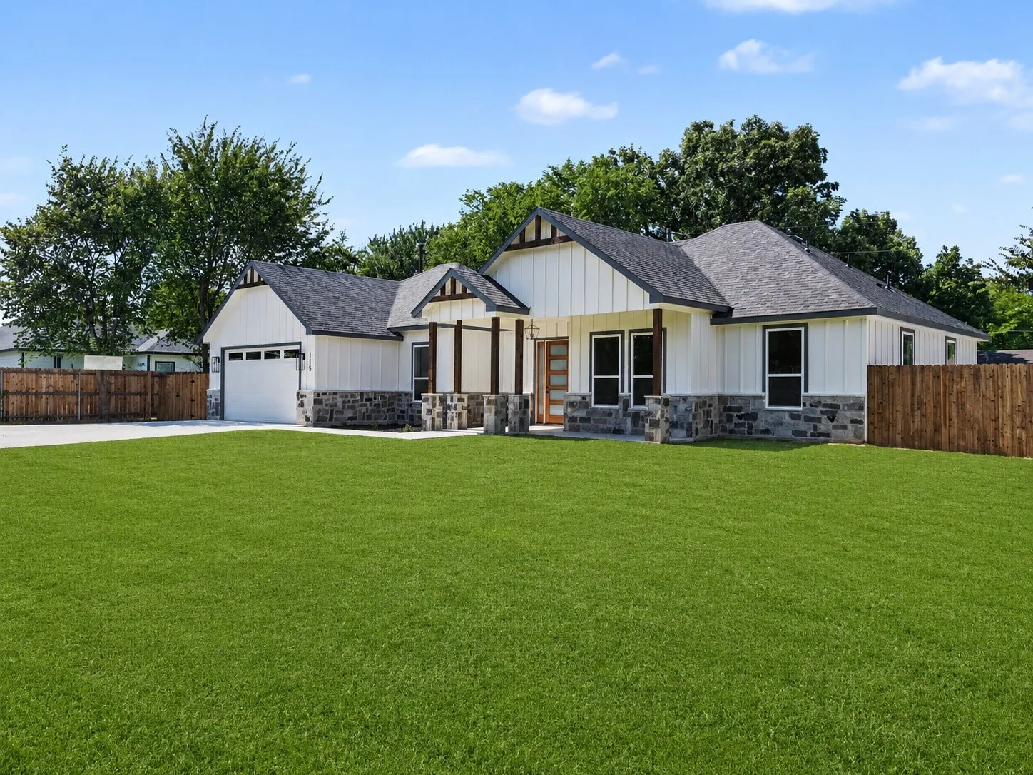 Modern farmhouse exterior featuring white vertical siding, dark shingle roofing, and stone veneer accents