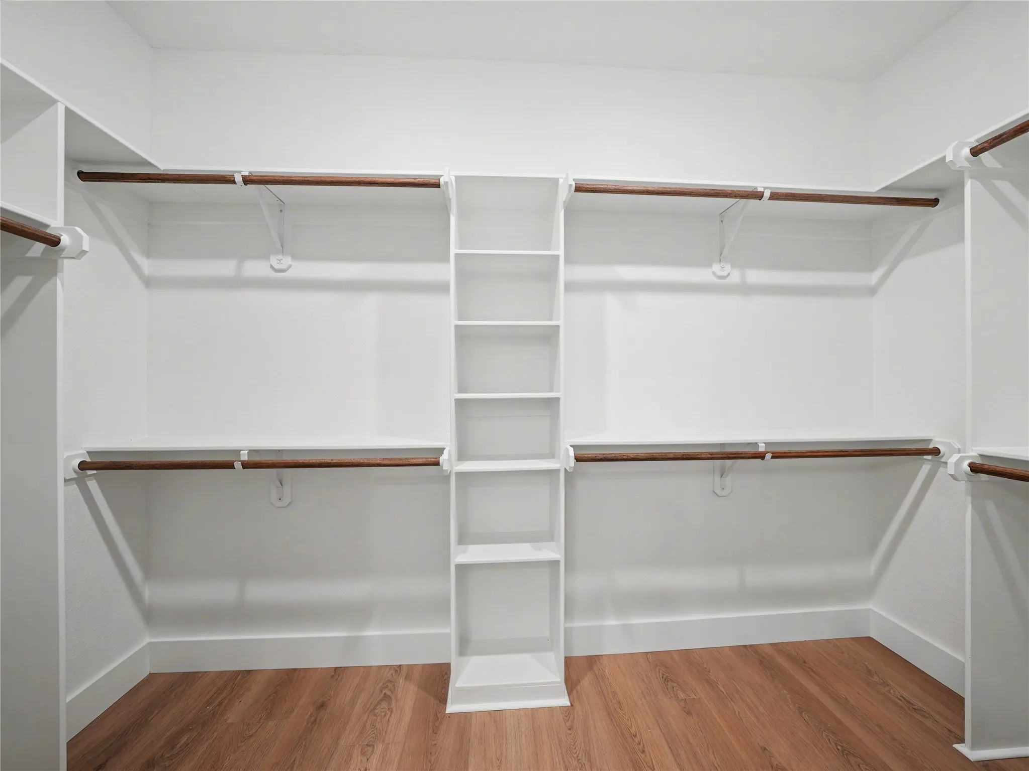 Walk-in closet featuring built-in shelving, multiple hanging rods, and wood-finish flooring
