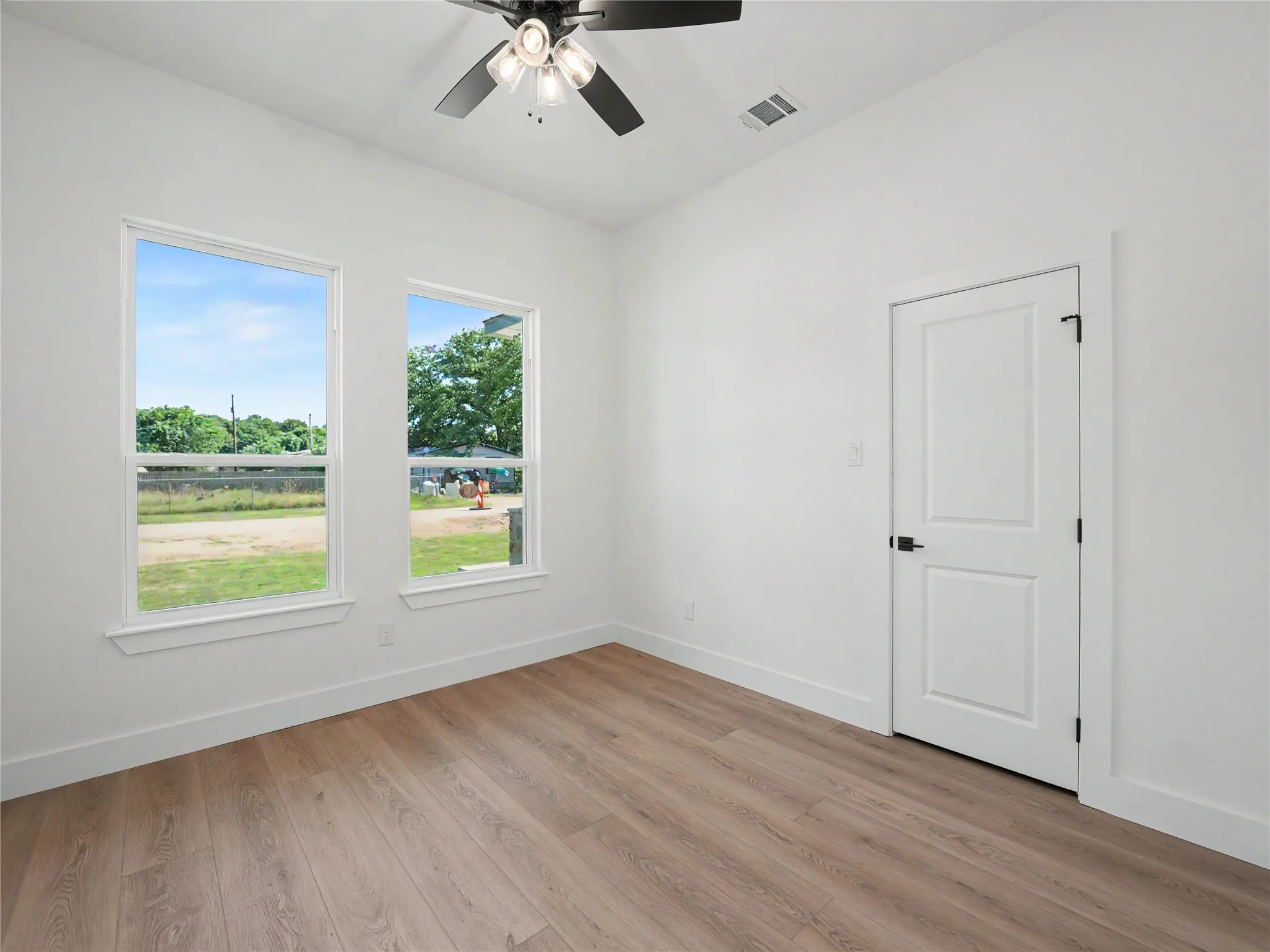 Interior room featuring wood-finish flooring, two large windows, a ceiling fan with light fixture, and a white paneled door with black hardware