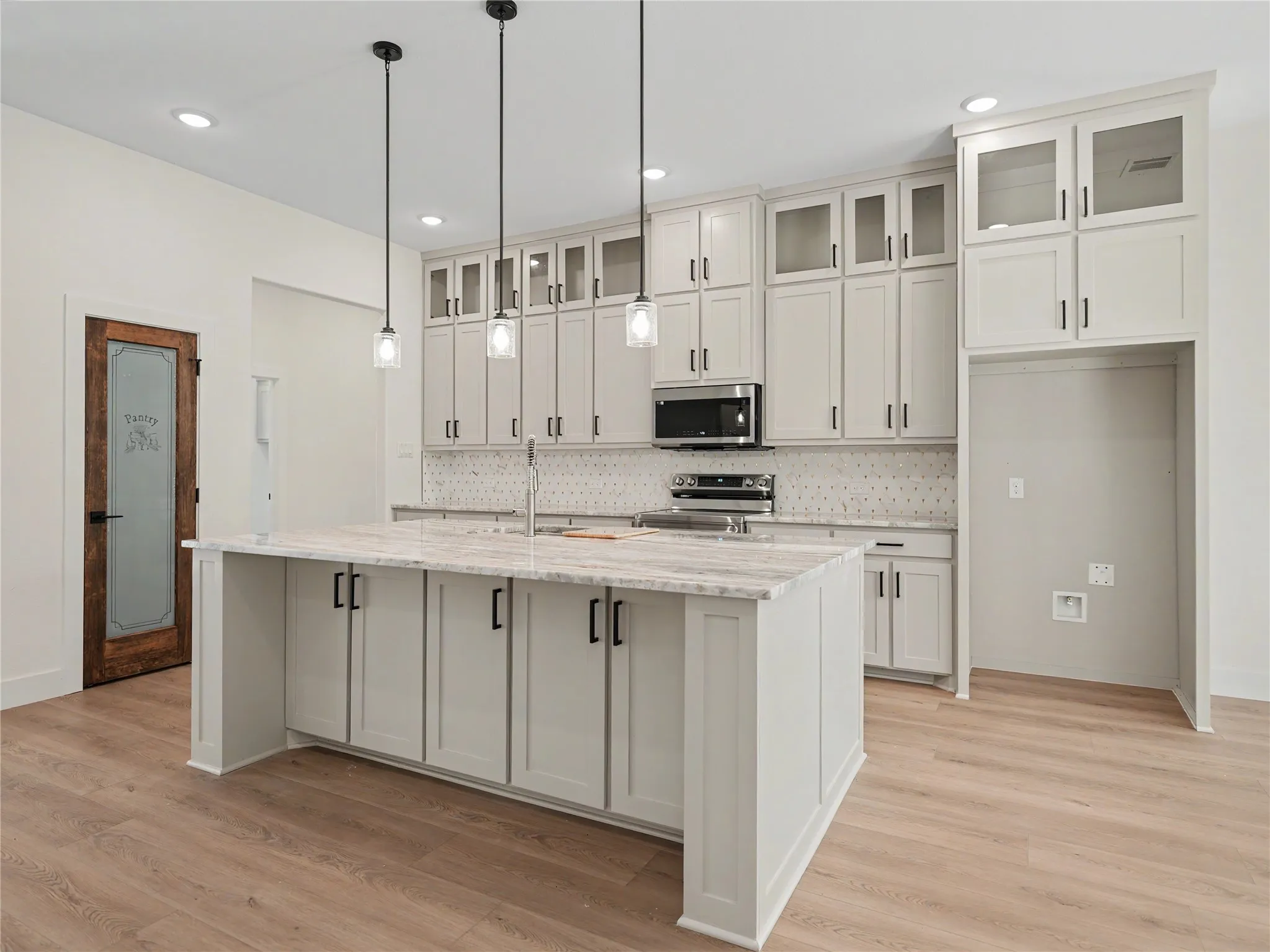 Kitchen featuring an expansive island with a stone countertop, abundant white cabinetry including glass-front uppers, a patterned tile backsplash, and wood-finish flooring