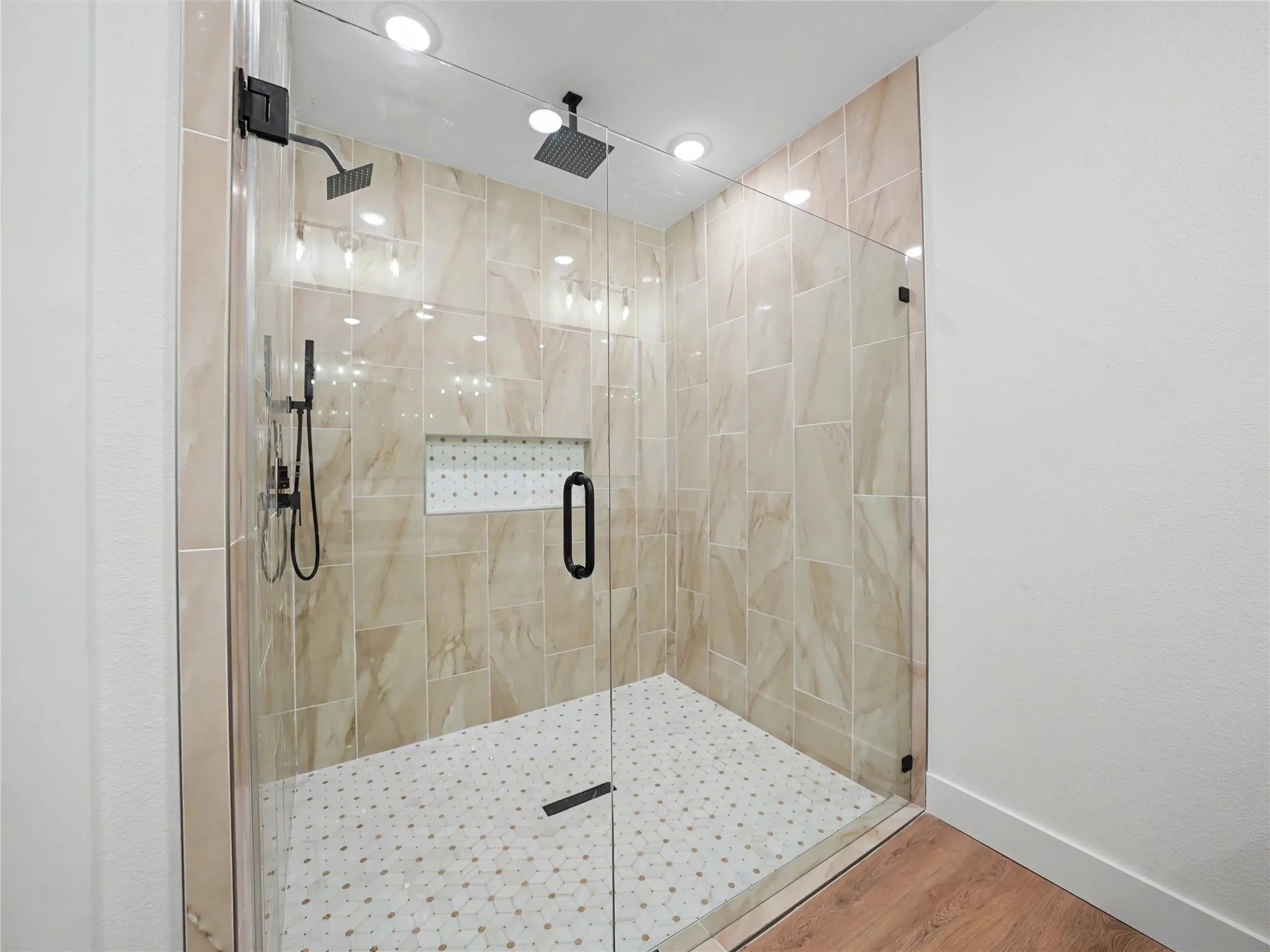 Glass-enclosed shower featuring floor-to-ceiling beige tile, a built-in tiled niche, and dual matte black showerheads