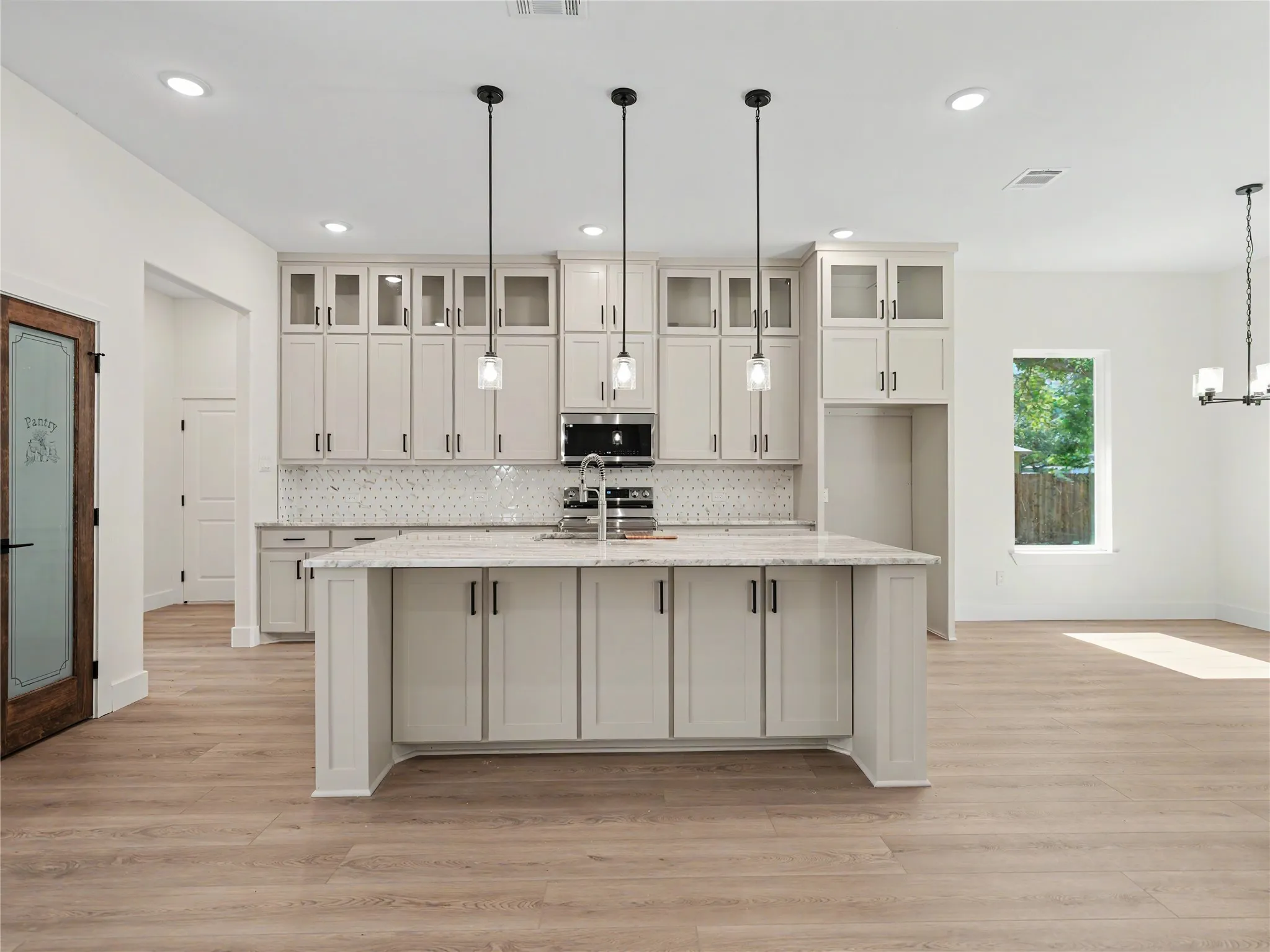 Kitchen featuring an expansive island with a built-in sink, stone countertop, pendant lighting, shaker-style cabinetry, and wood-finish flooring