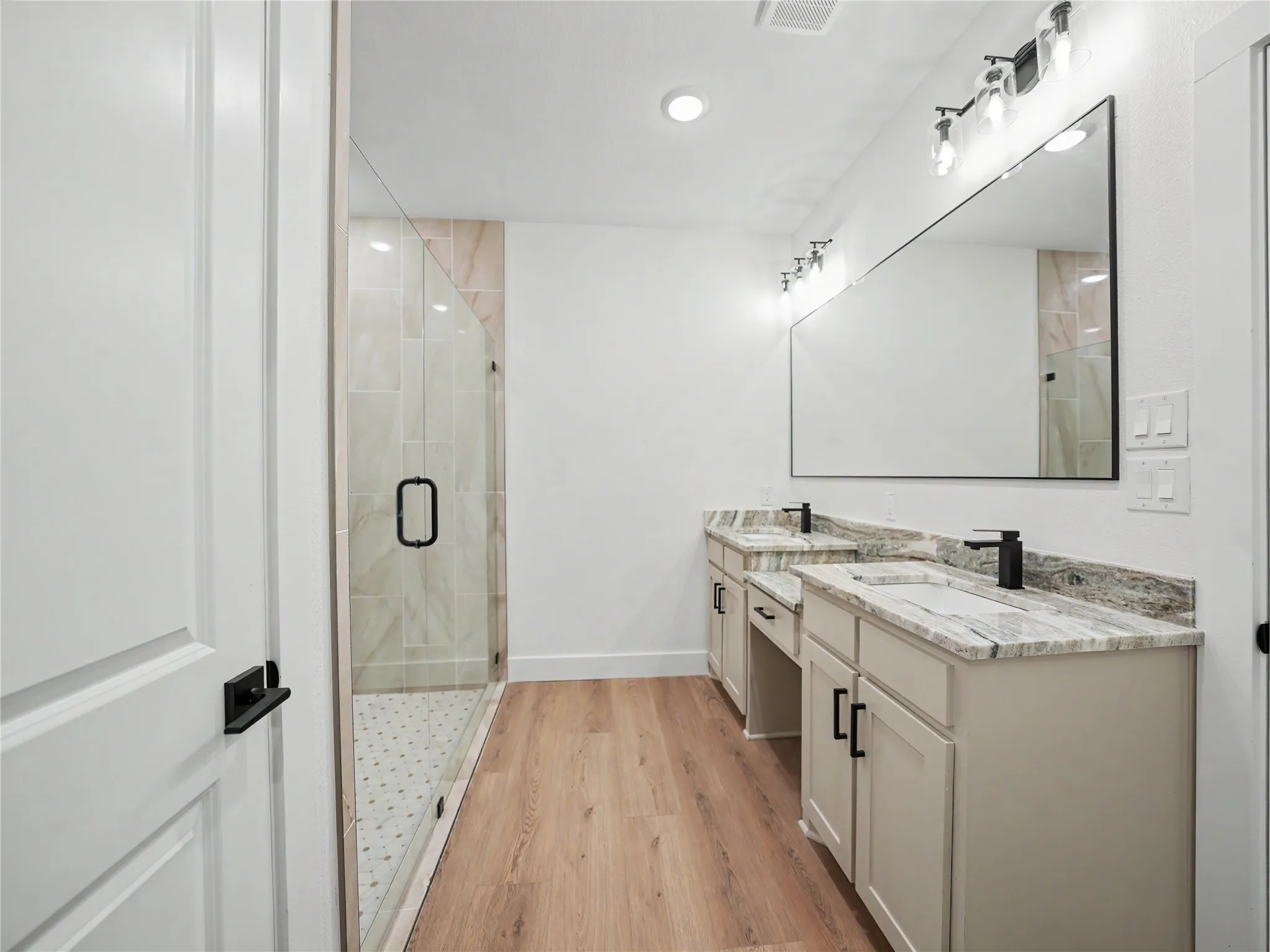 Spacious bathroom featuring a dual vanity with stone countertops, a large frameless mirror, and modern black fixtures