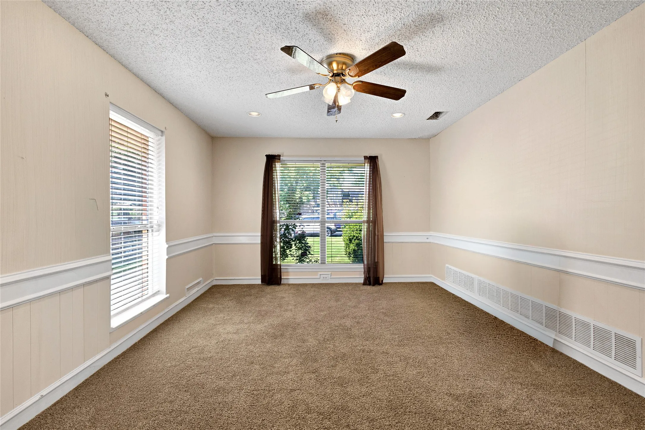 Spacious room featuring neutral carpeting, chair rail molding, and a ceiling fan with integrated lighting