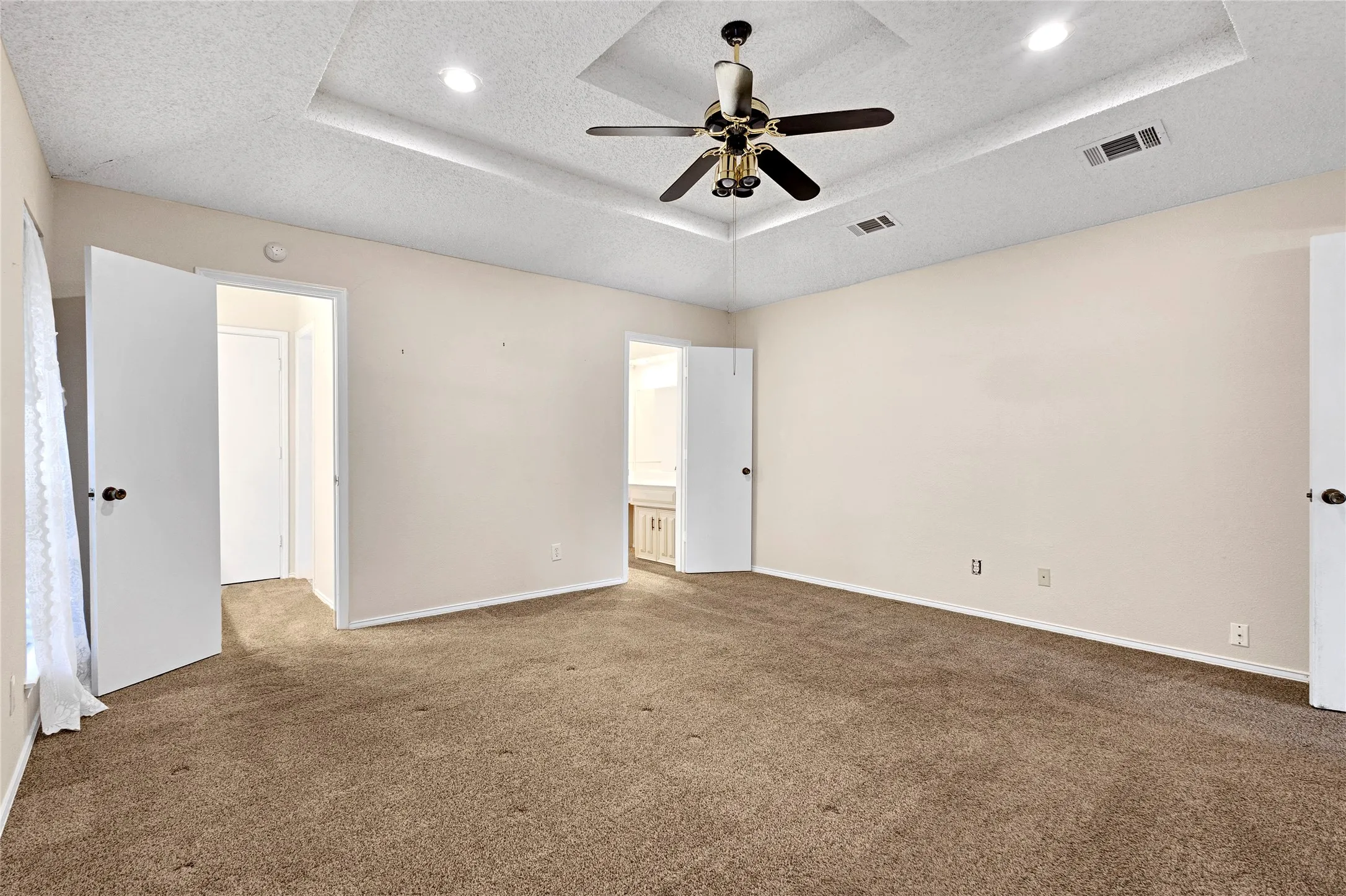 Spacious room featuring a tray ceiling with recessed lighting and ceiling fan