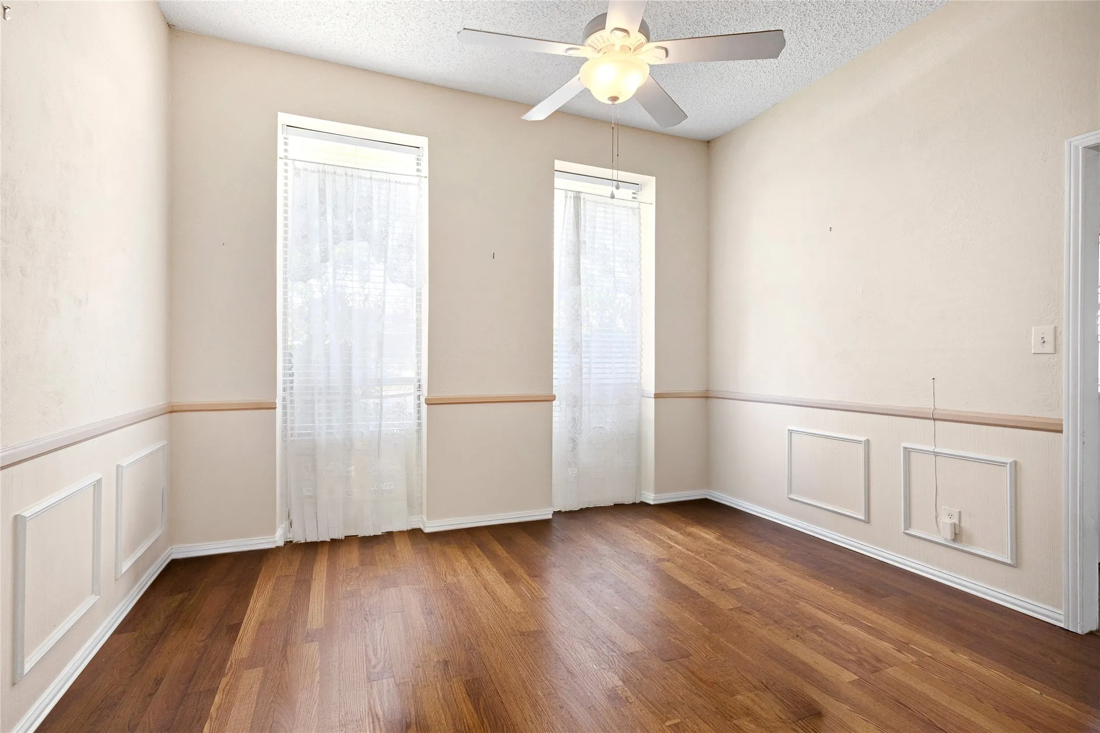 Vaulted ceiling space featuring wood-finish flooring, wainscoting, and a ceiling fan with integrated lighting