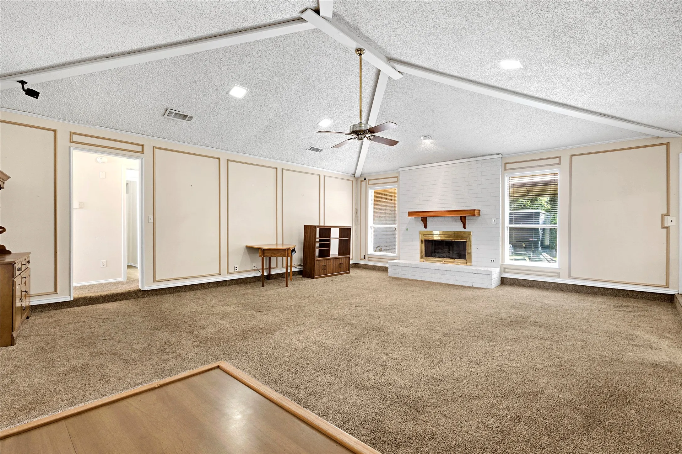 Spacious living area featuring a vaulted ceiling with exposed beams, an overhead fan, and recessed lighting