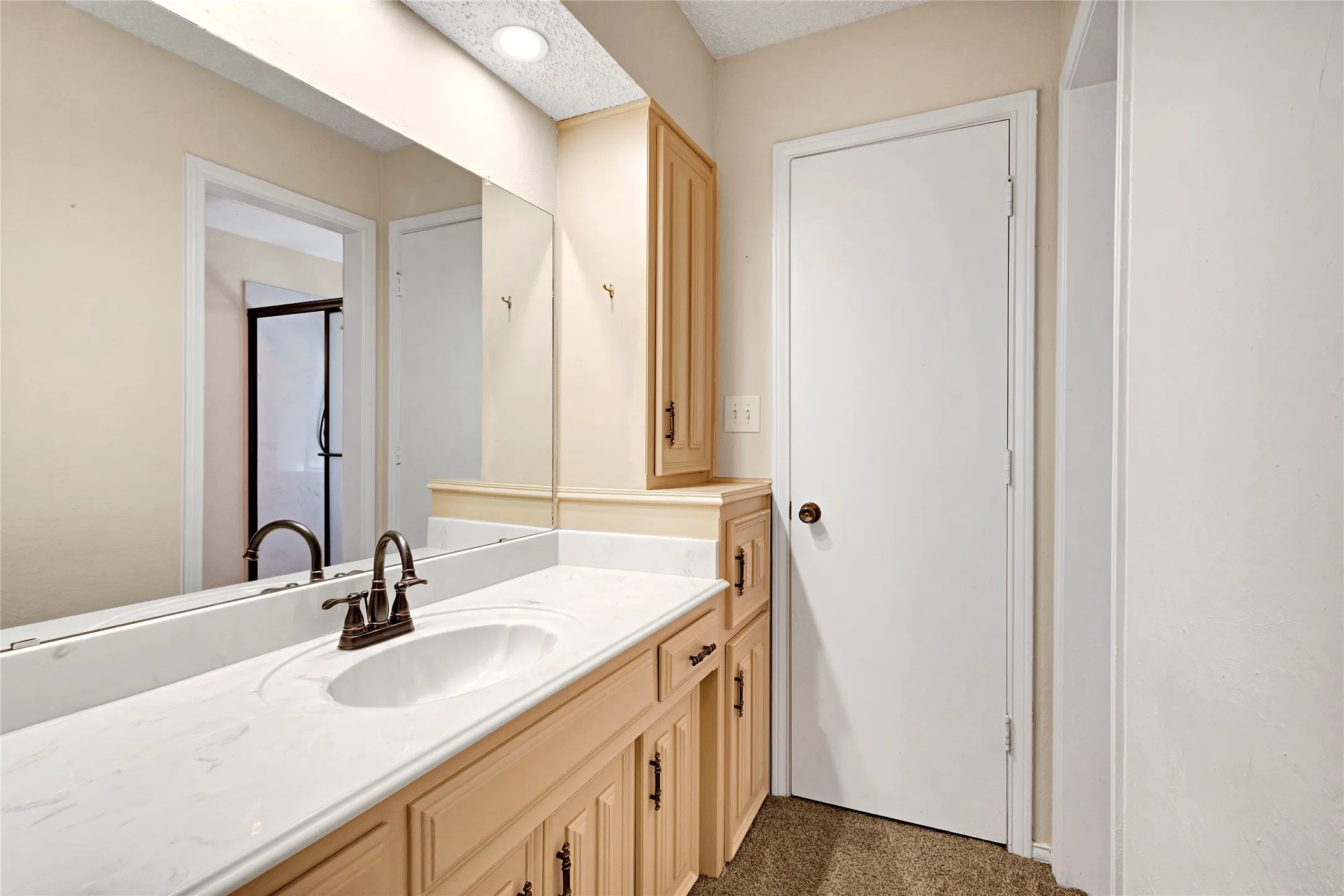 Double vanity with a white countertop and integrated sinks, wood-finish cabinetry, bronze-finish fixtures, and full-width mirror