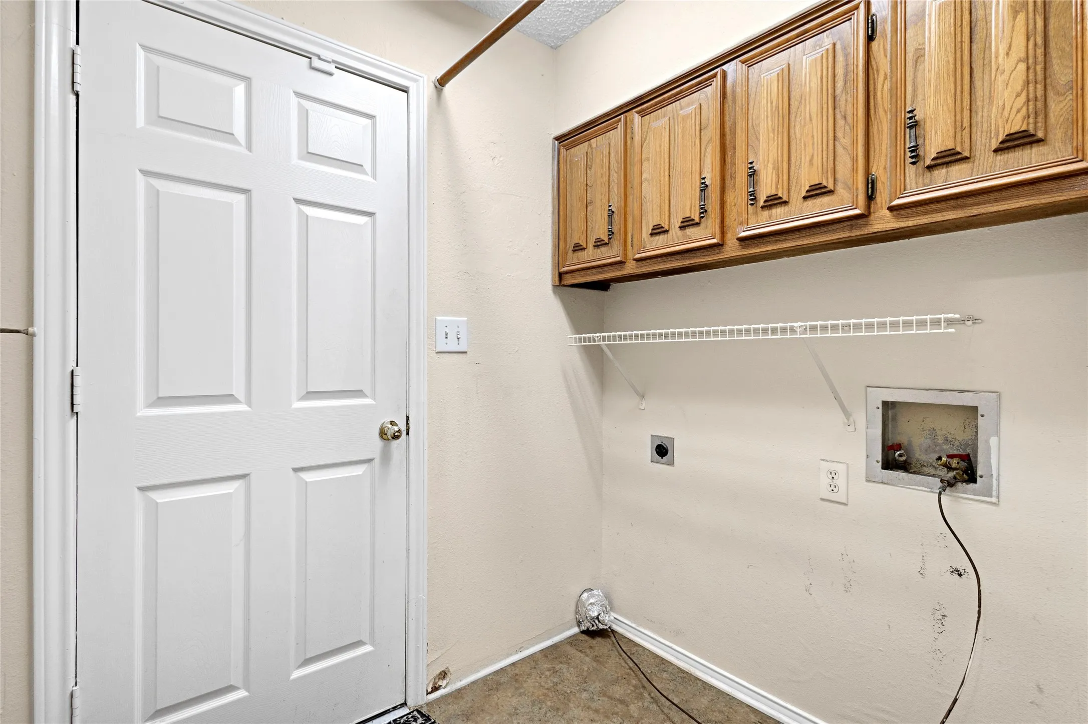 Utility space featuring overhead wood-finish cabinetry, a wire shelf, and light-colored wall paint