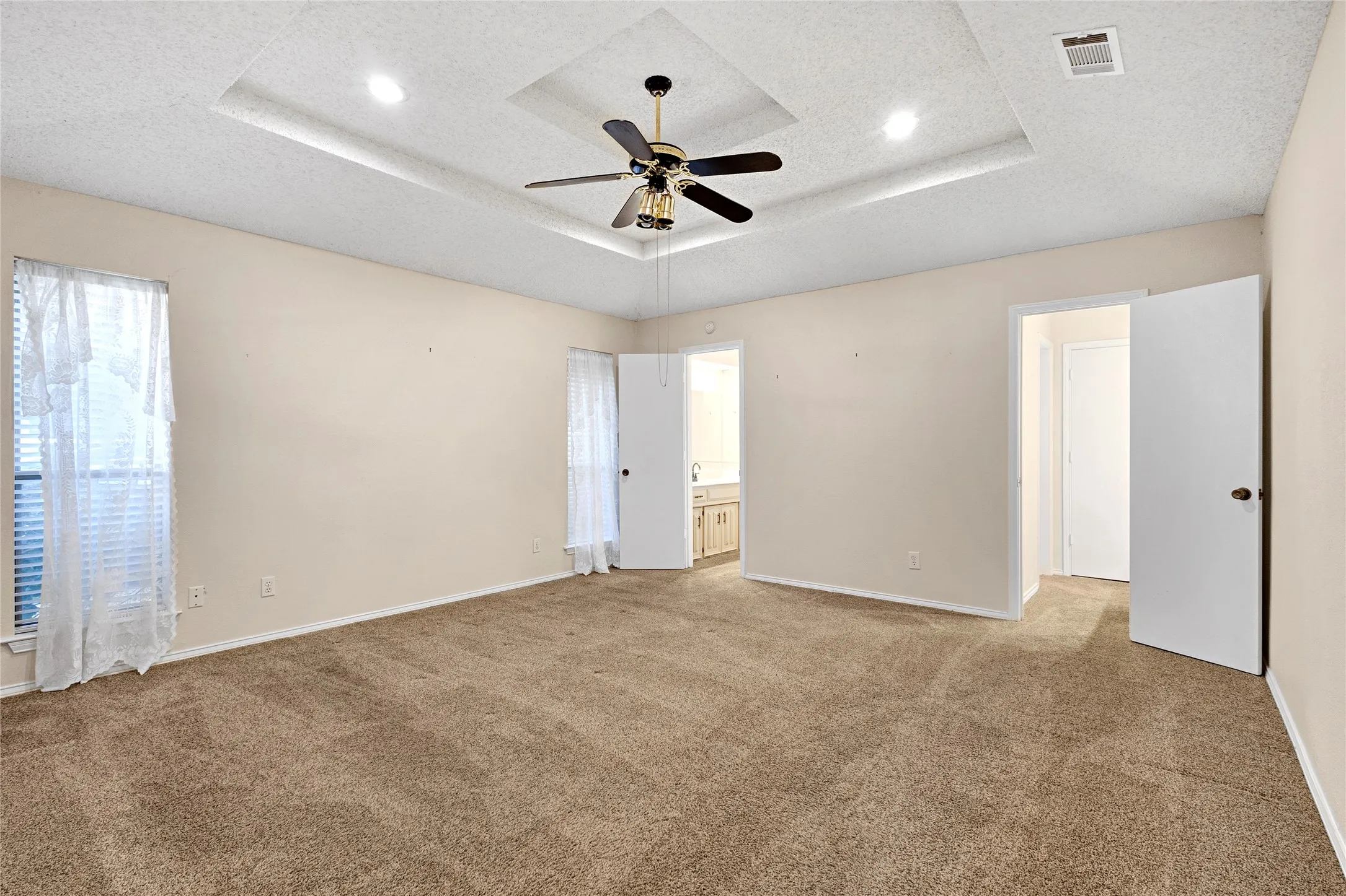 Expansive room featuring a recessed tray ceiling with an integrated ceiling fan and recessed lighting