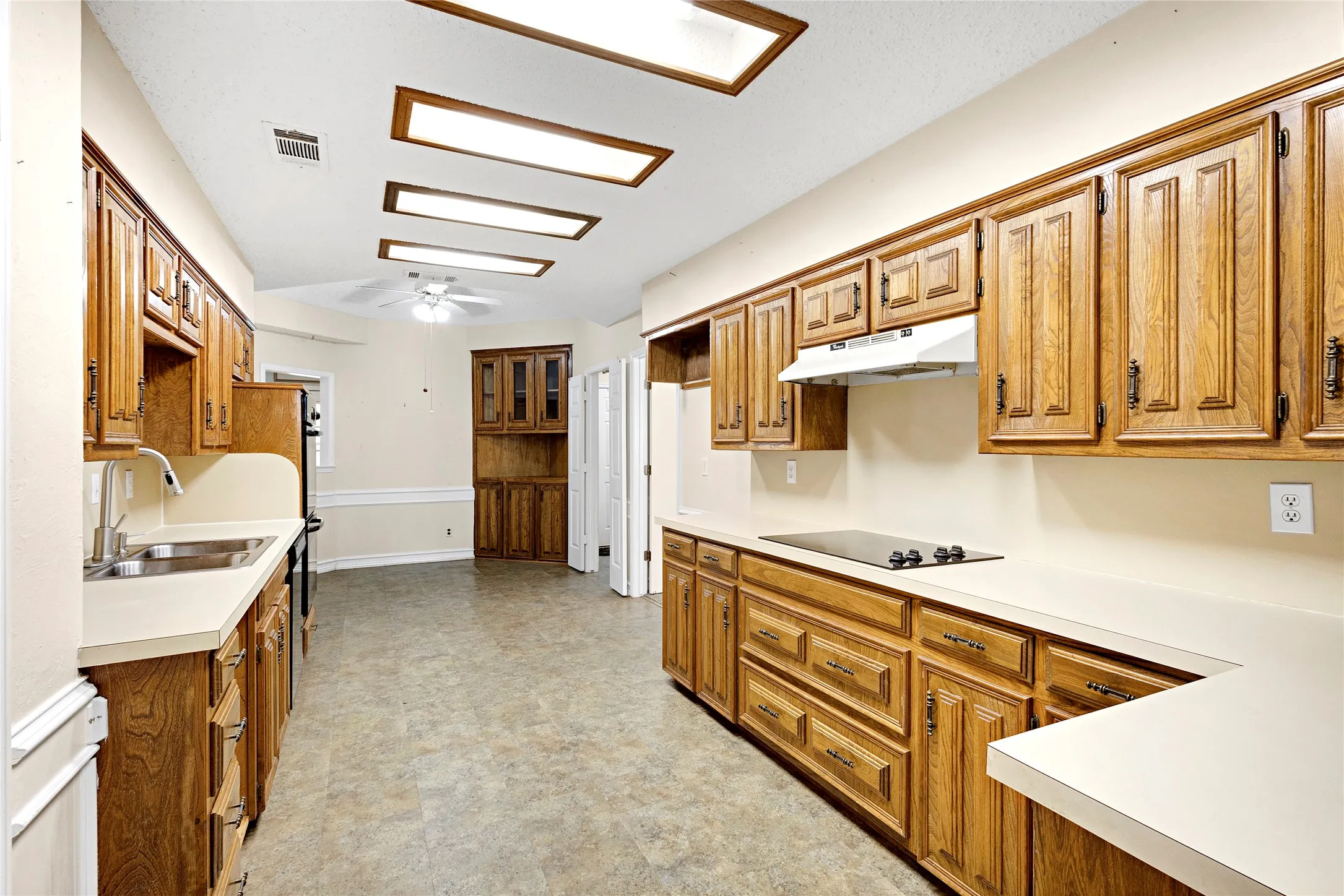 Kitchen featuring abundant wood cabinetry, light-toned countertops, and a built-in cooktop with overhead ventilation