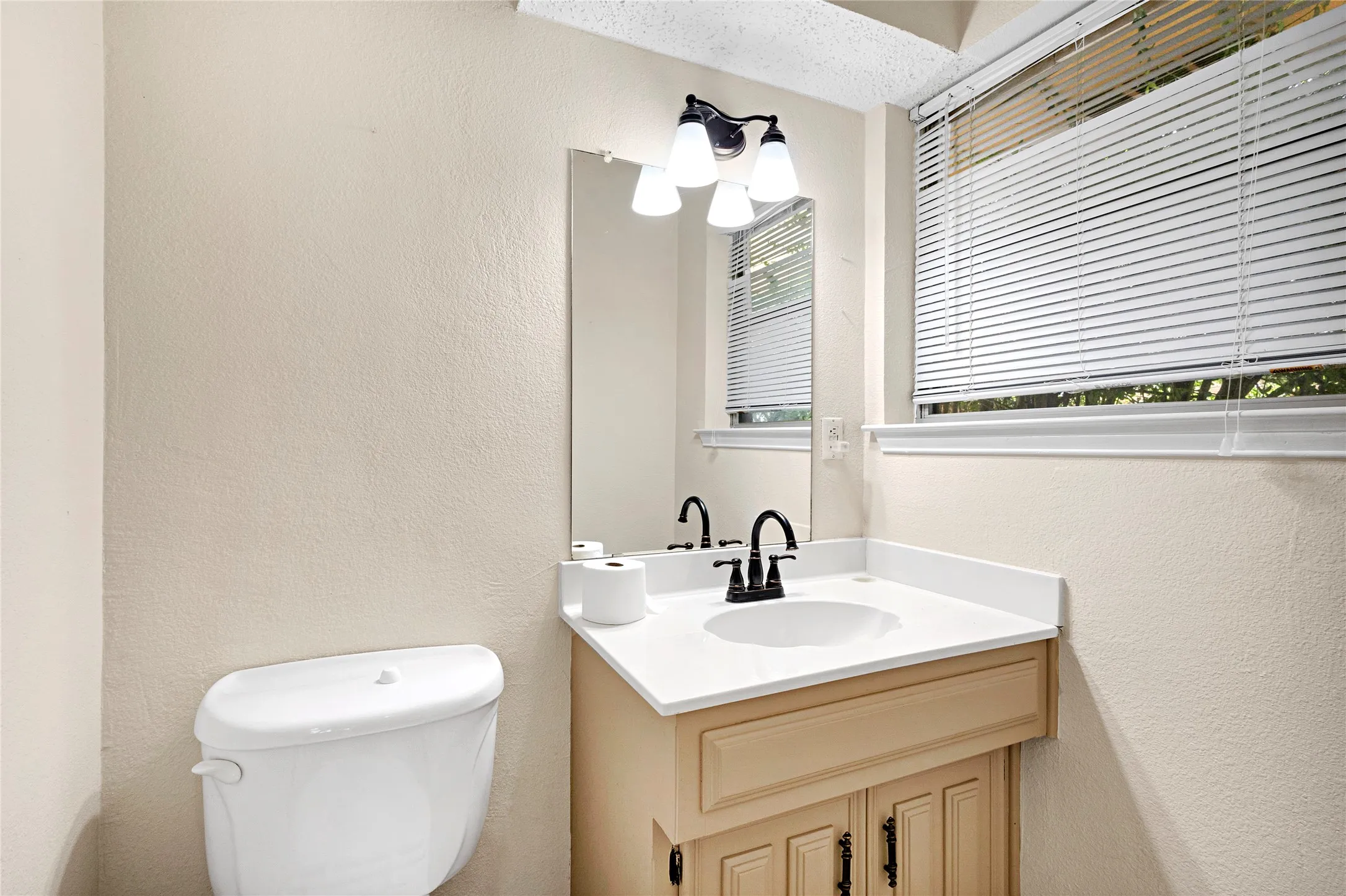 Bathroom featuring a vanity with a white countertop and integrated sink, a dark bronze faucet, and a wall-mounted light fixture