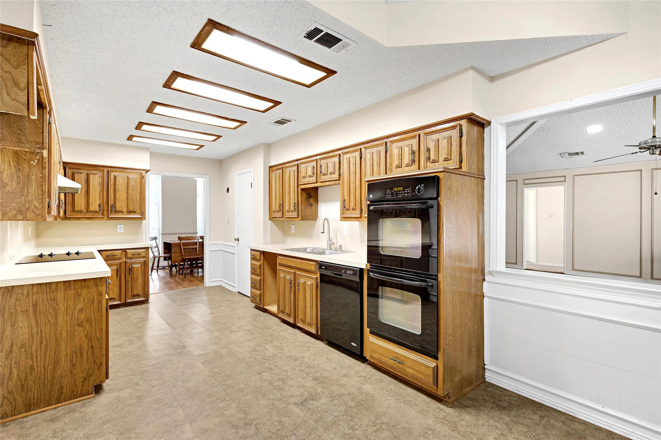 Kitchen featuring wood cabinetry, white countertops, black double wall ovens, built-in black dishwasher, and a black cooktop