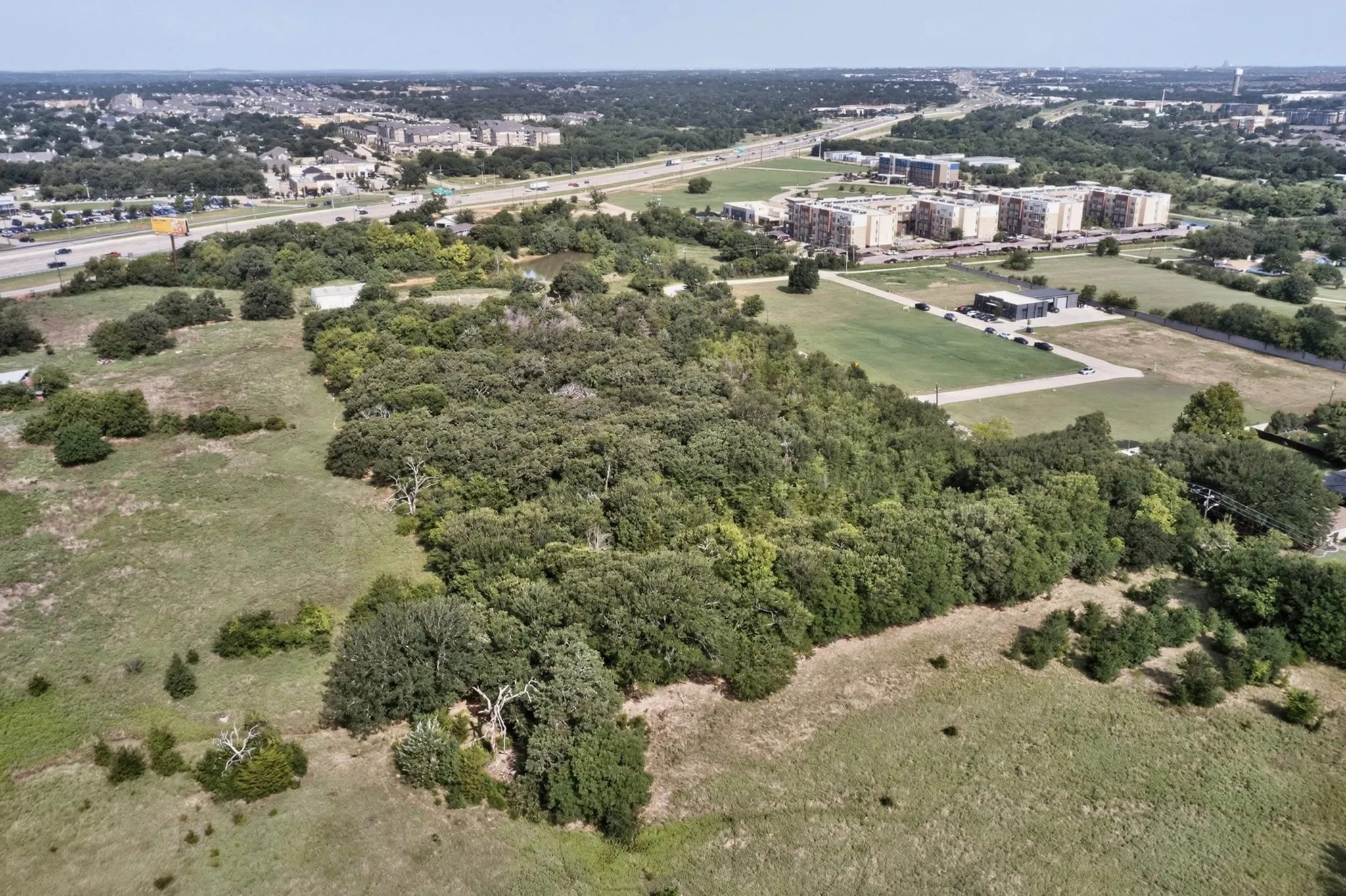 Expansive land parcel featuring mature tree coverage, open grassy areas, and proximity to highway infrastructure