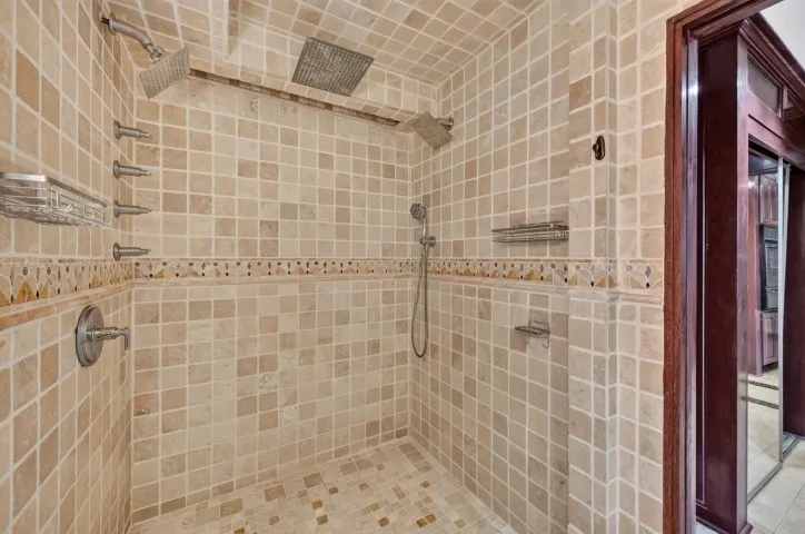 Tiled shower enclosure featuring a ceiling-mounted rainfall showerhead, wall-mounted showerhead, and multiple body sprayers