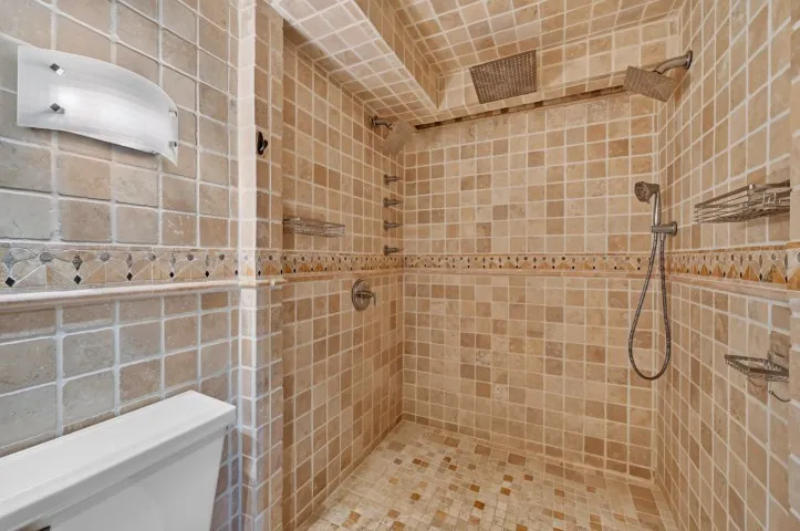 Tiled shower enclosure featuring dual showerheads, a handheld shower fixture, and recessed shelving