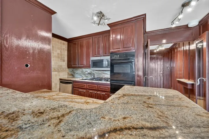 Spacious kitchen featuring a large granite-finish peninsula, rich wood cabinetry, stainless steel microwave, black double wall oven, and a tiled backsplash