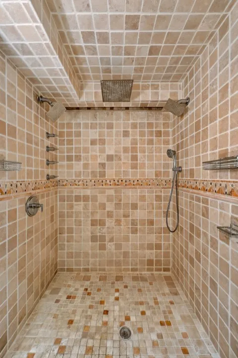 Tiled shower with a rain shower head, multiple wall-mounted shower heads, and an integrated handheld shower