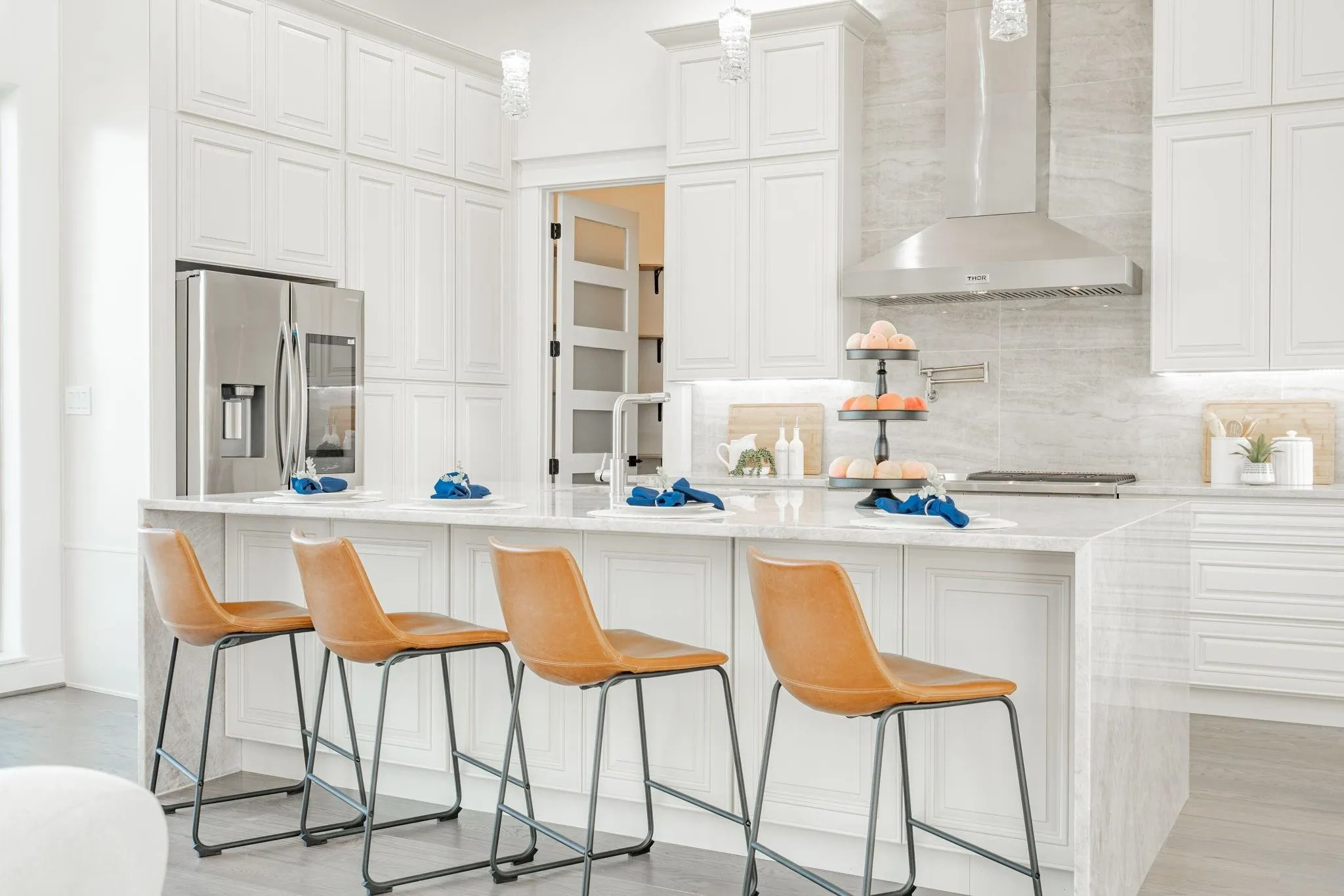 Modern kitchen featuring white shaker cabinetry, stainless steel appliances, a large center island with a light-toned countertop, and a full-height backsplash